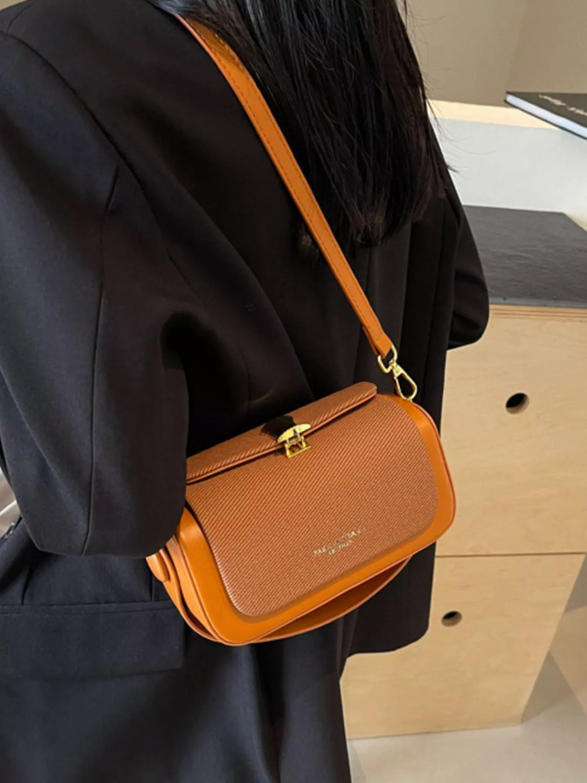 Brown flap crossbody bag with gold-tone hardware and adjustable strap on shoulder