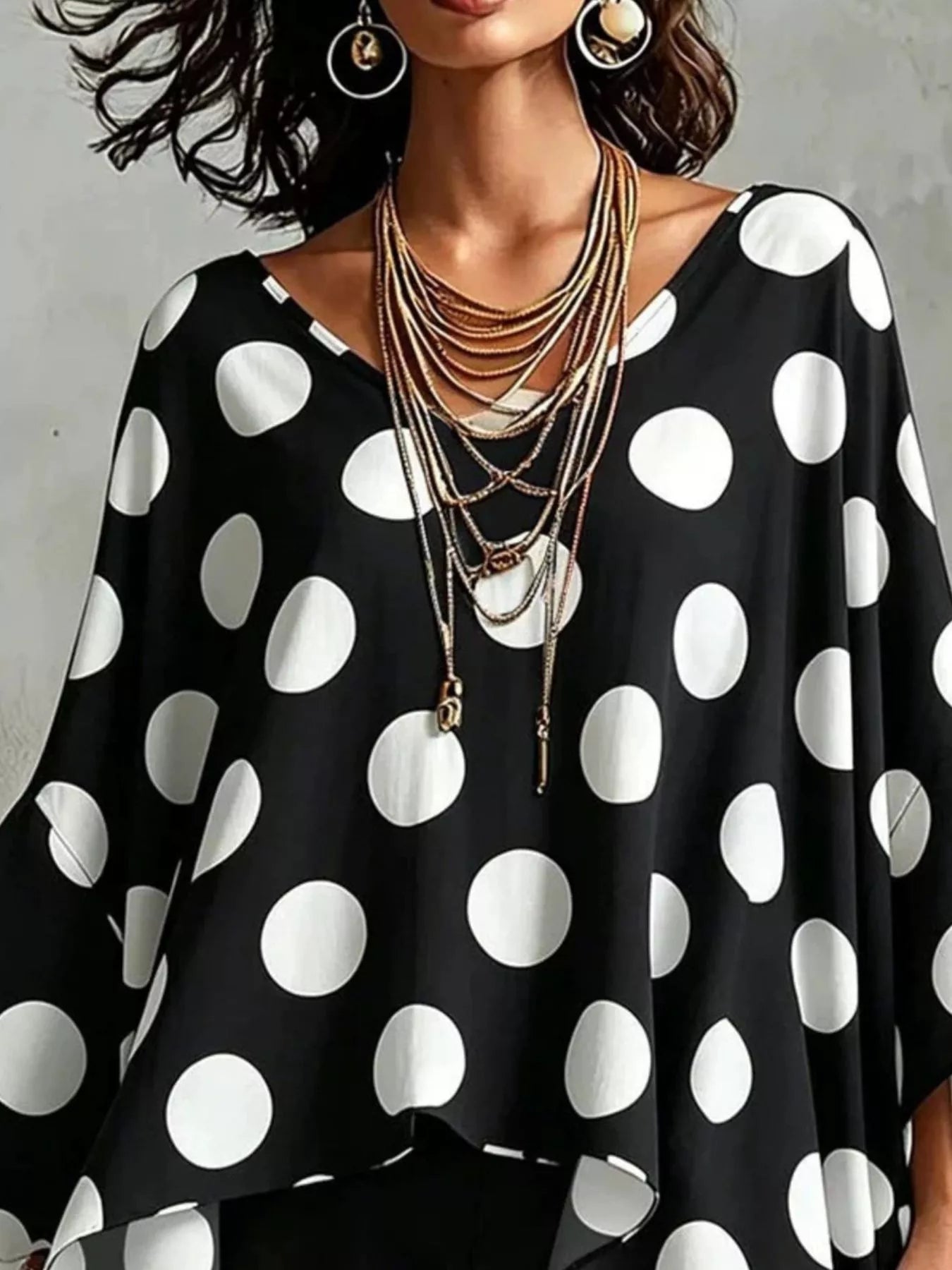 Black polka dot asymmetrical hem blouse with relaxed drape and wide round neckline.
