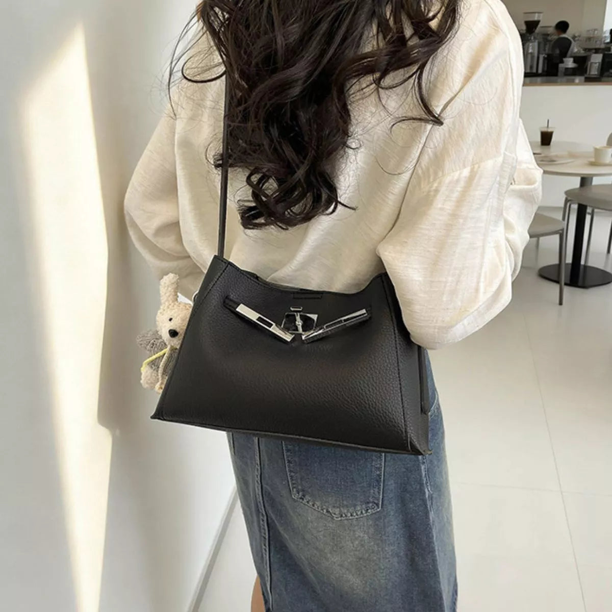 Black crossbody bag with silver lock clasp, structured shape; worn over shoulder