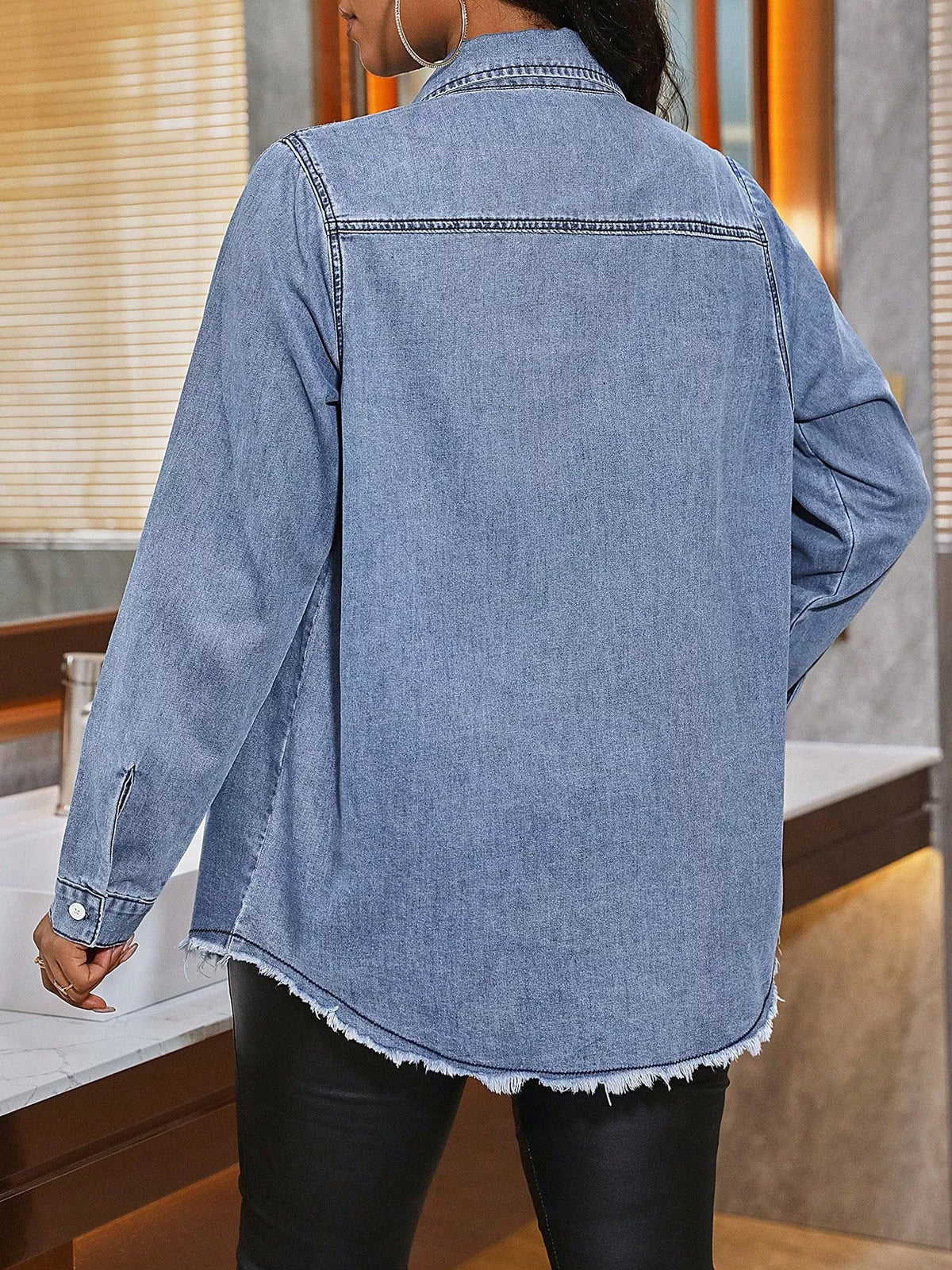 Back view: light-wash denim button-up shirt with curved raw hem and long sleeves