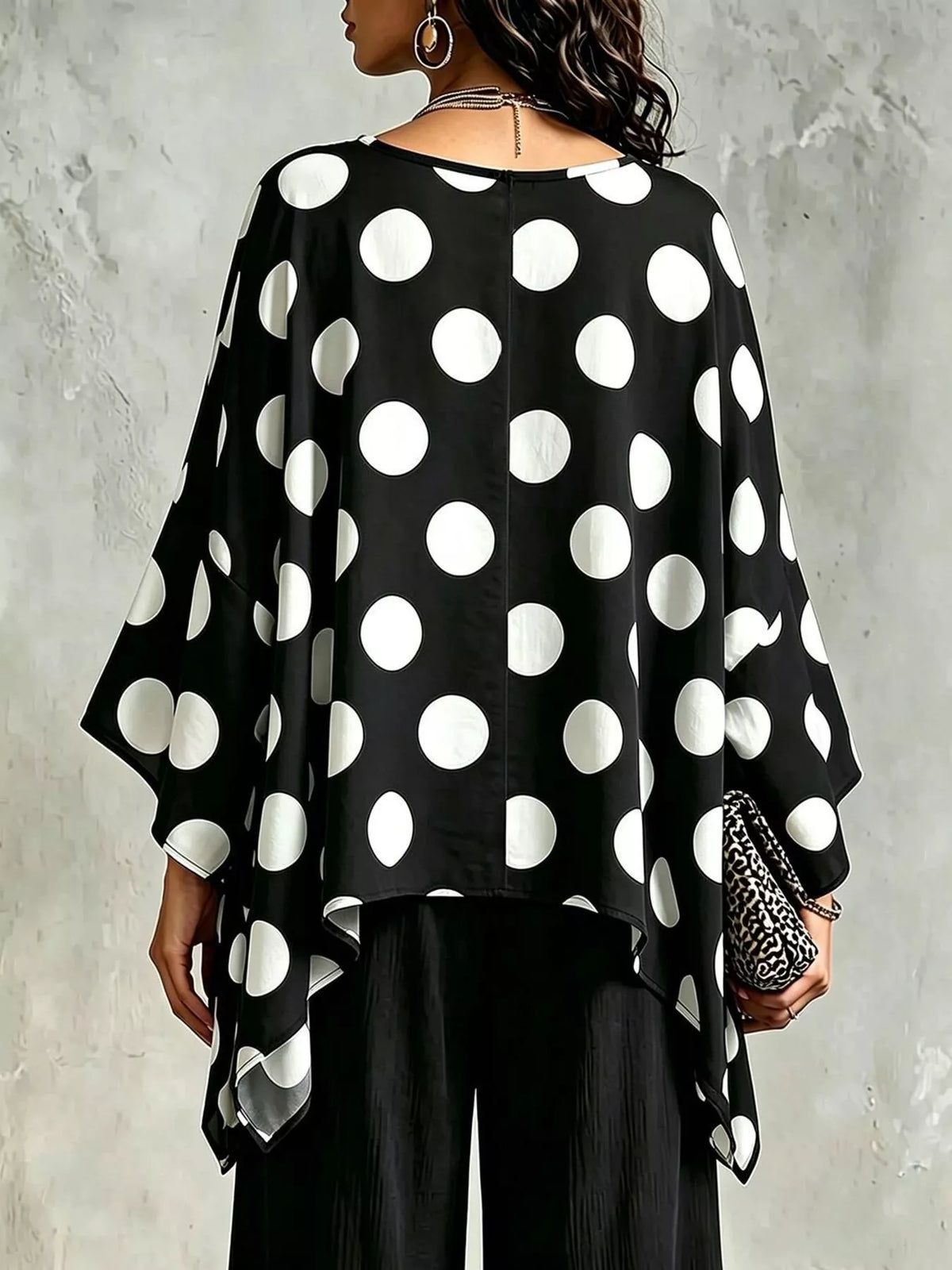 Black polka dot asymmetrical hem blouse, back view with draped batwing sleeves.
