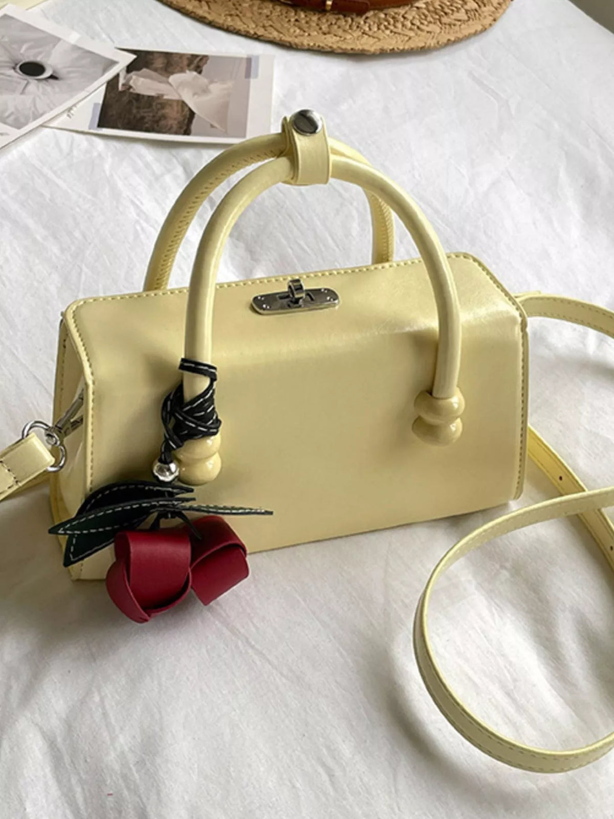 Yellow top-handle crossbody bag with curved handles, front clasp, crossbody strap, ribbon charm