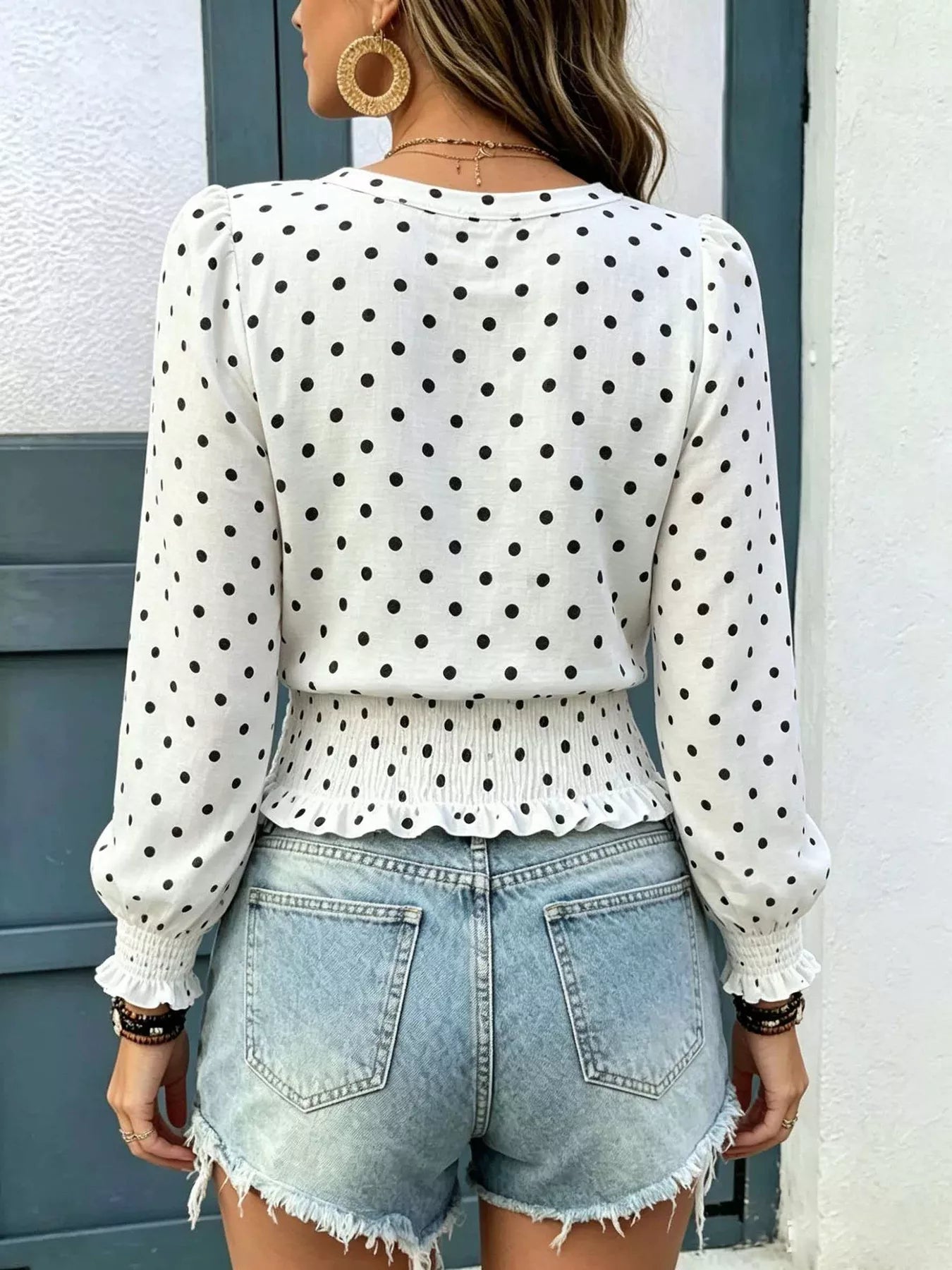 White polka dot long-sleeve smocked blouse with V-neck and peplum-style ruffle hem