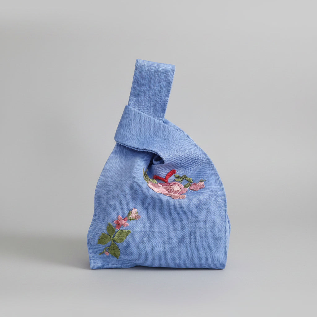 Knot wrist bag in blue with floral embroidery patch and knotted top handle.
