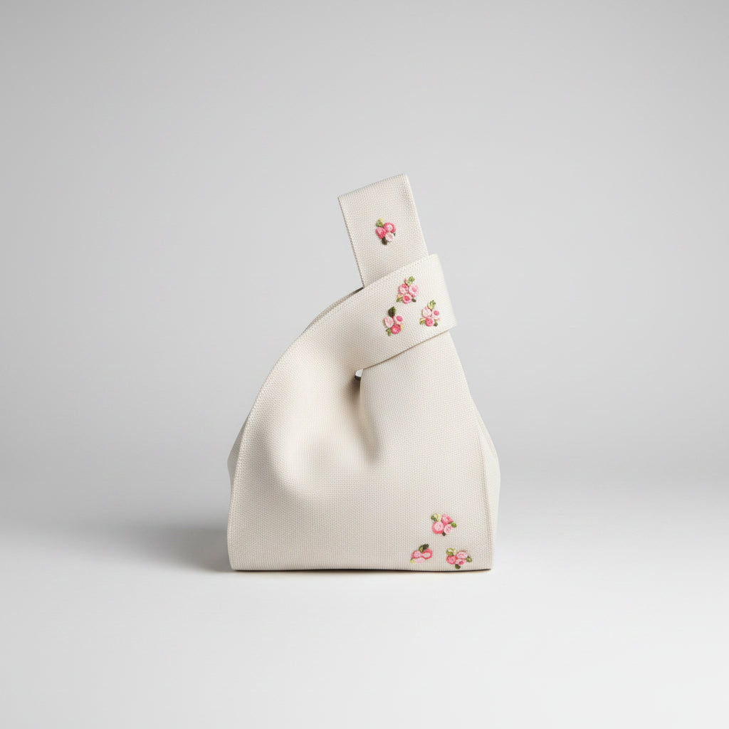 Ivory knot wrist bag with small pink floral embroidery on front and strap