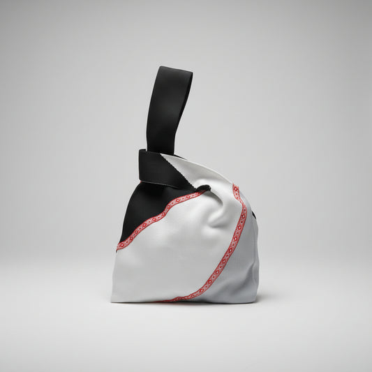 Knot wrist bag in white fabric with red trim and black handle strap.