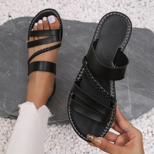 Black open-toe flat sandals with wide toe straps and braided ankle tie