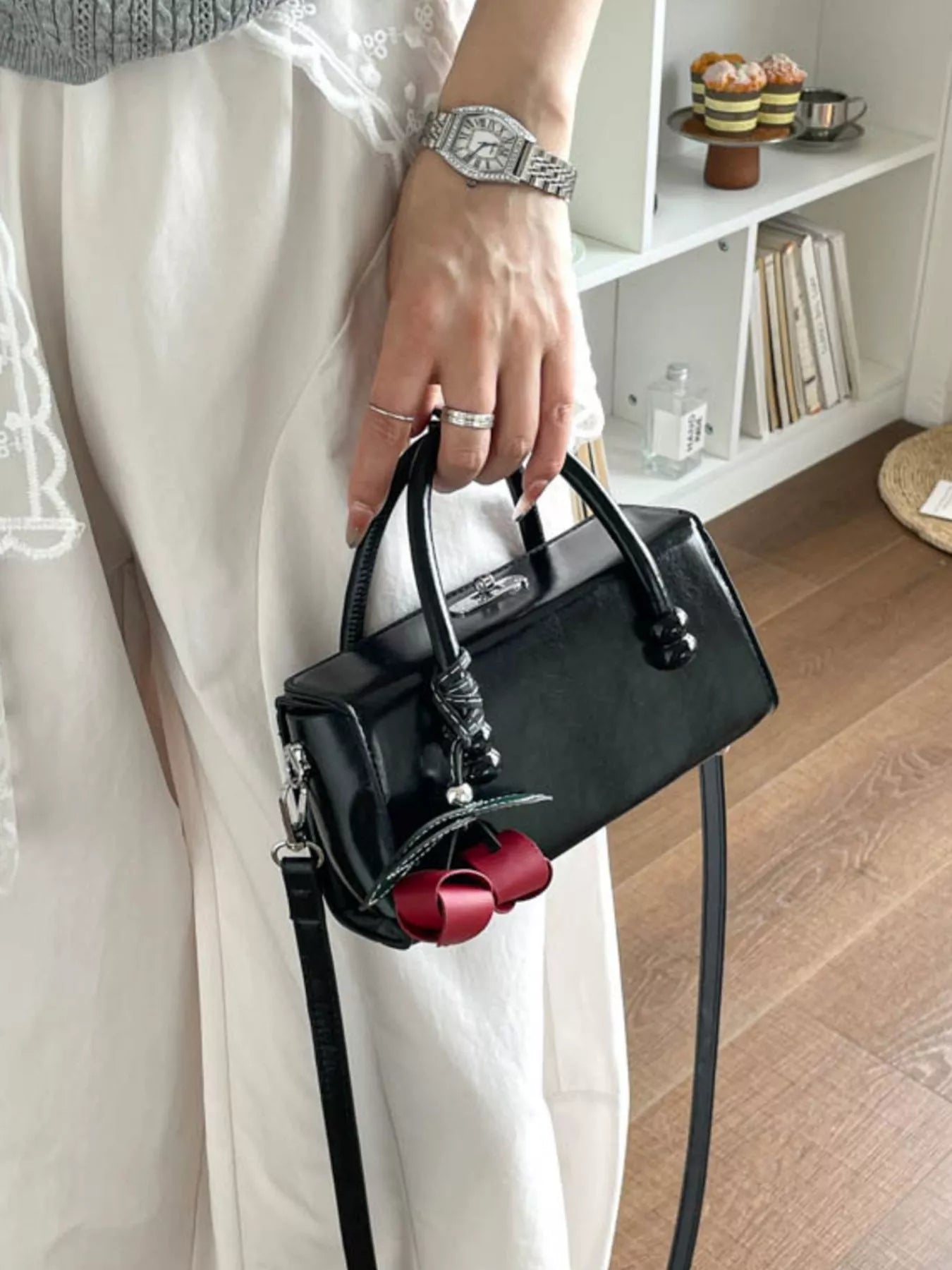 Black top-handle crossbody bag with long strap and red bow keychain charm.