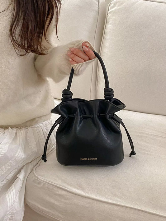 Black drawstring bucket crossbody bag with bow-tied front and round top opening