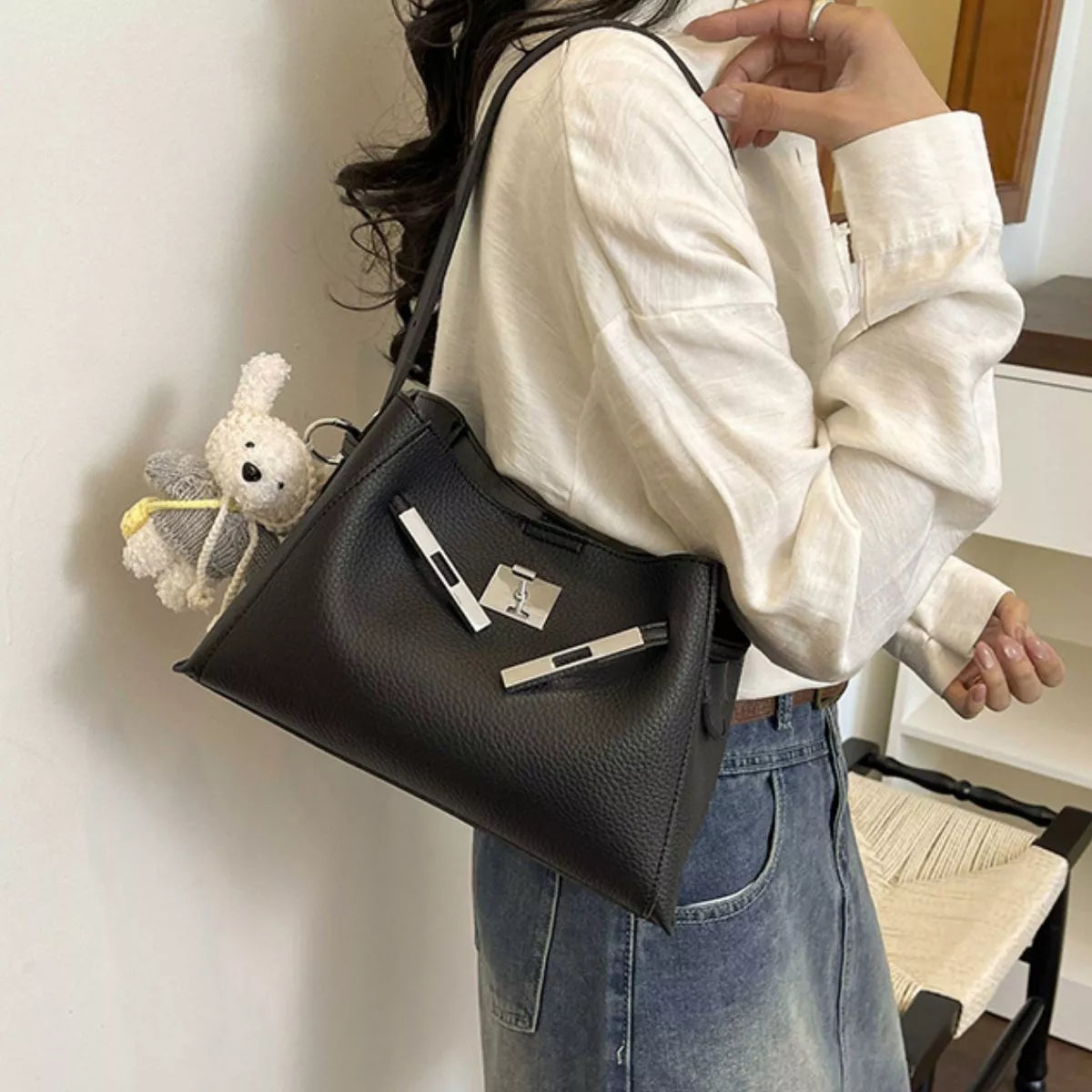 Black crossbody bag with silver lock front, top zip, and teddy charm; worn on model
