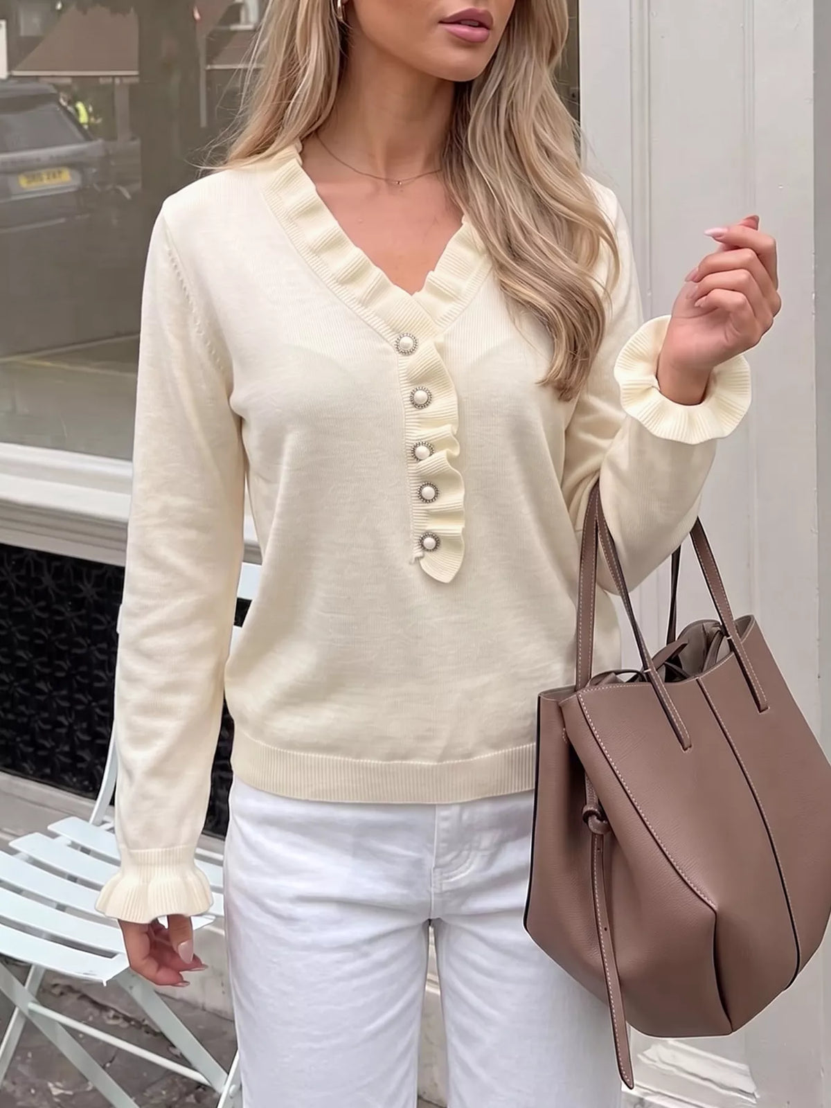 Cream knit V-neck top featuring ruffled neckline and pearl-look button front