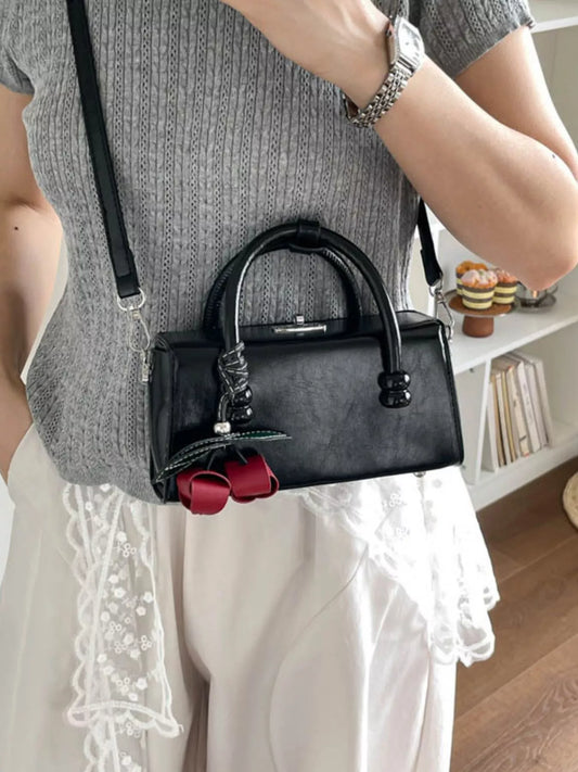 Black top-handle crossbody bag with shiny hardware and red bow charm.