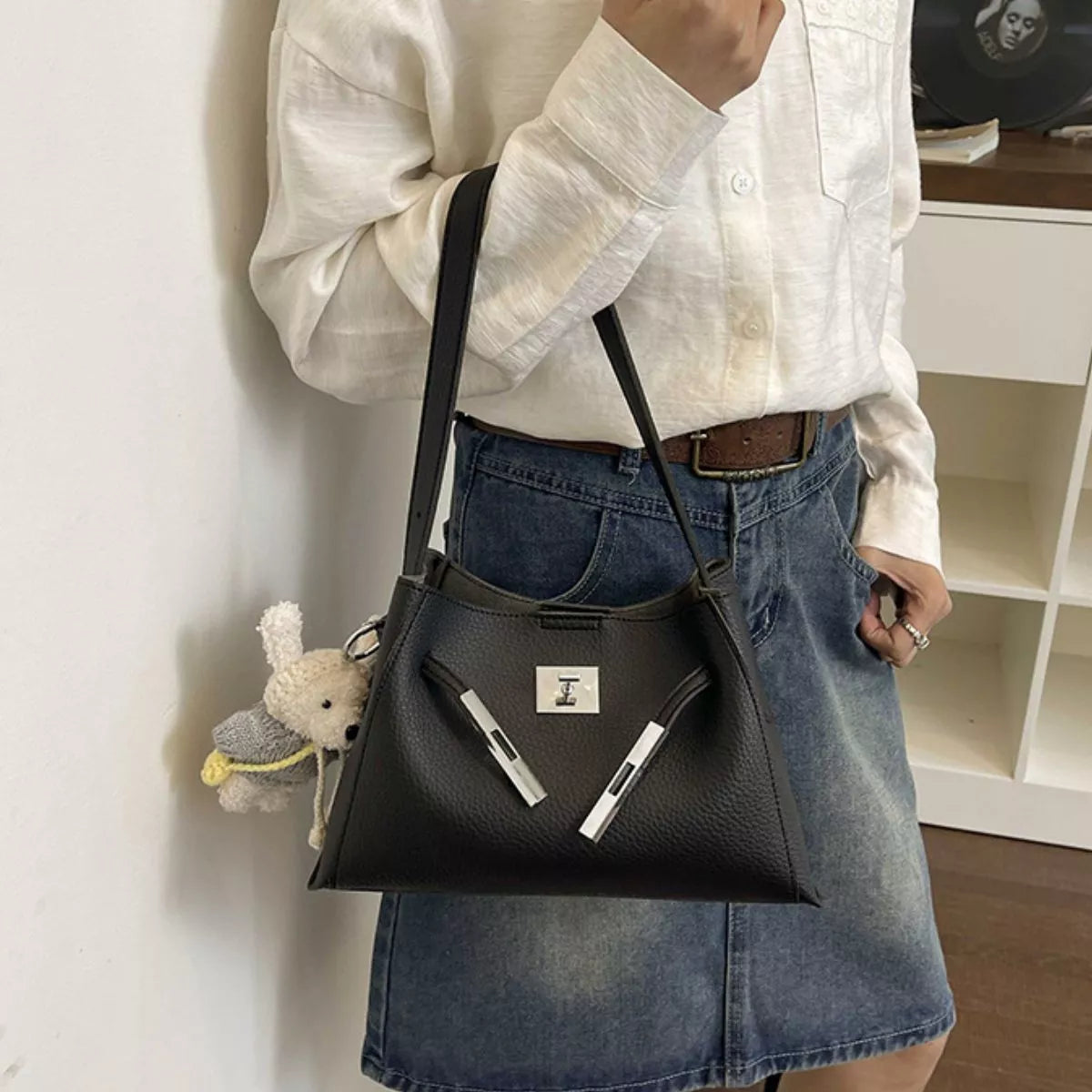 Black crossbody bag with silver lock hardware and top zip opening; styled with denim skirt
