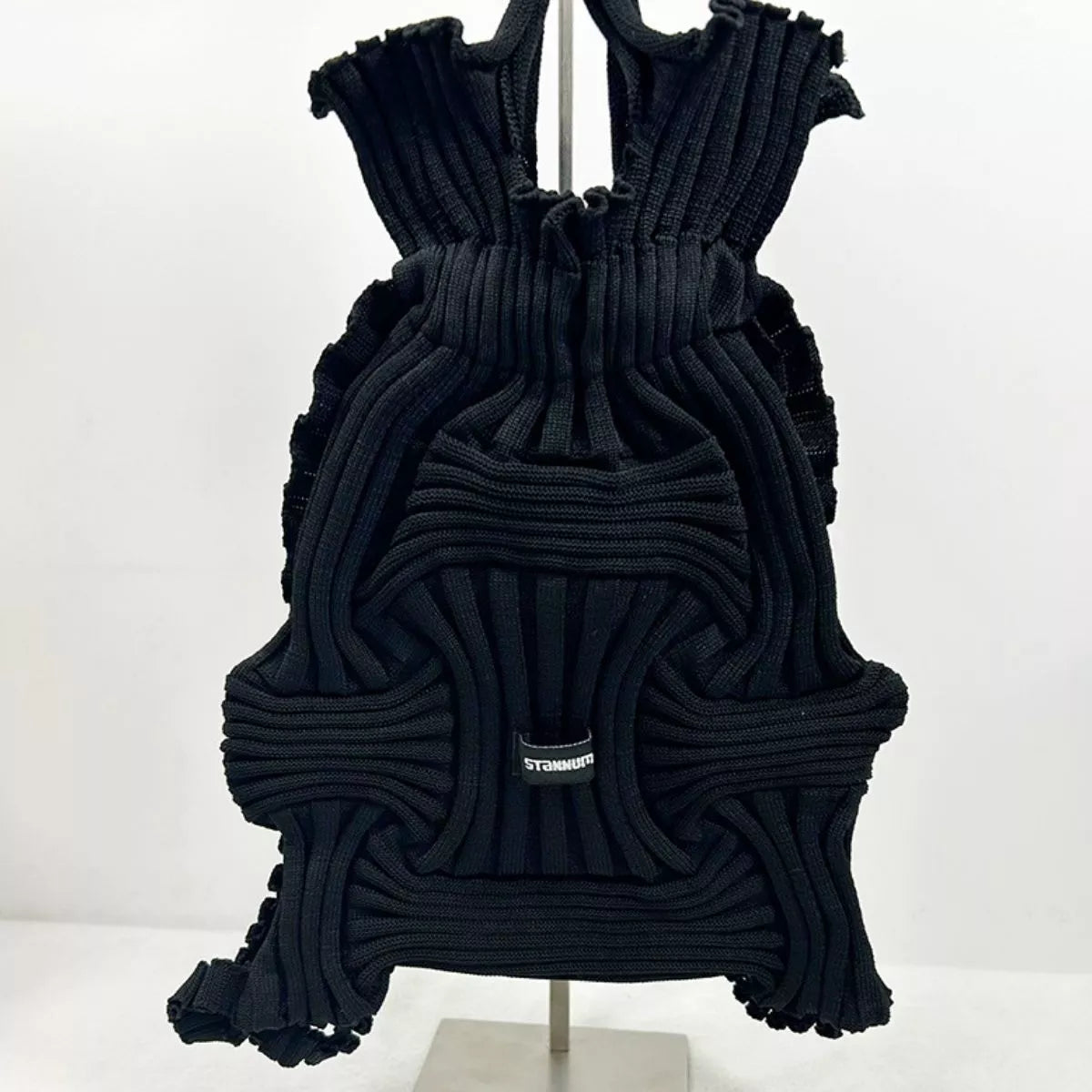 Black textured knit backpack bag with ruffled layers, top handles, front patch logo