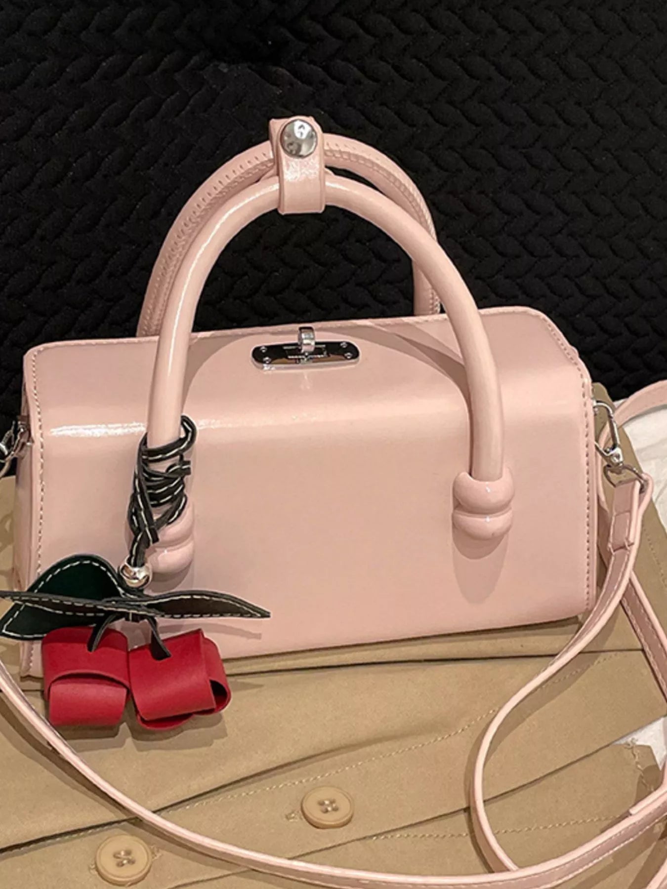 Light pink top-handle crossbody bag with crossbody strap and red bow charm.