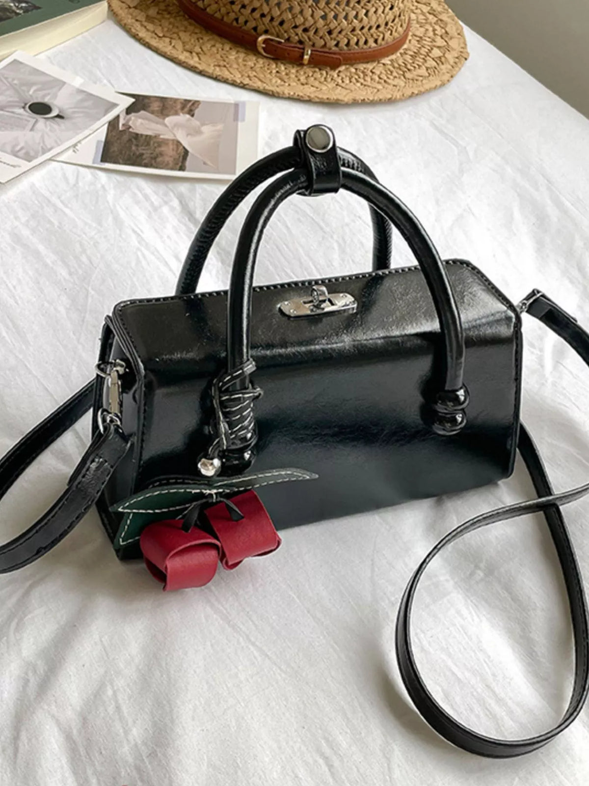 Black top-handle crossbody bag with crossbody strap and red bow charm.