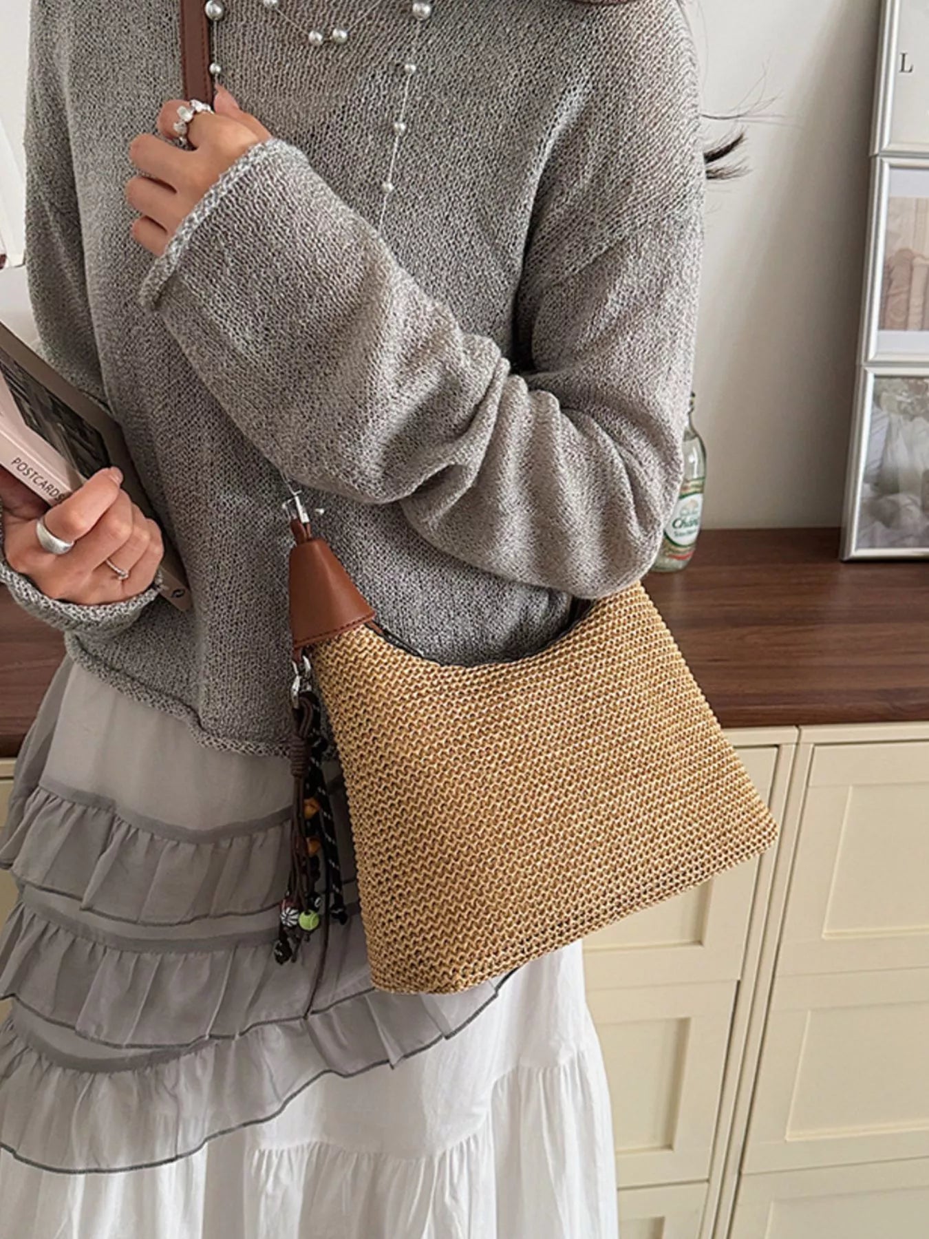 Straw crossbody bag in tan with brown leather handle and braided strap, woven texture detail
