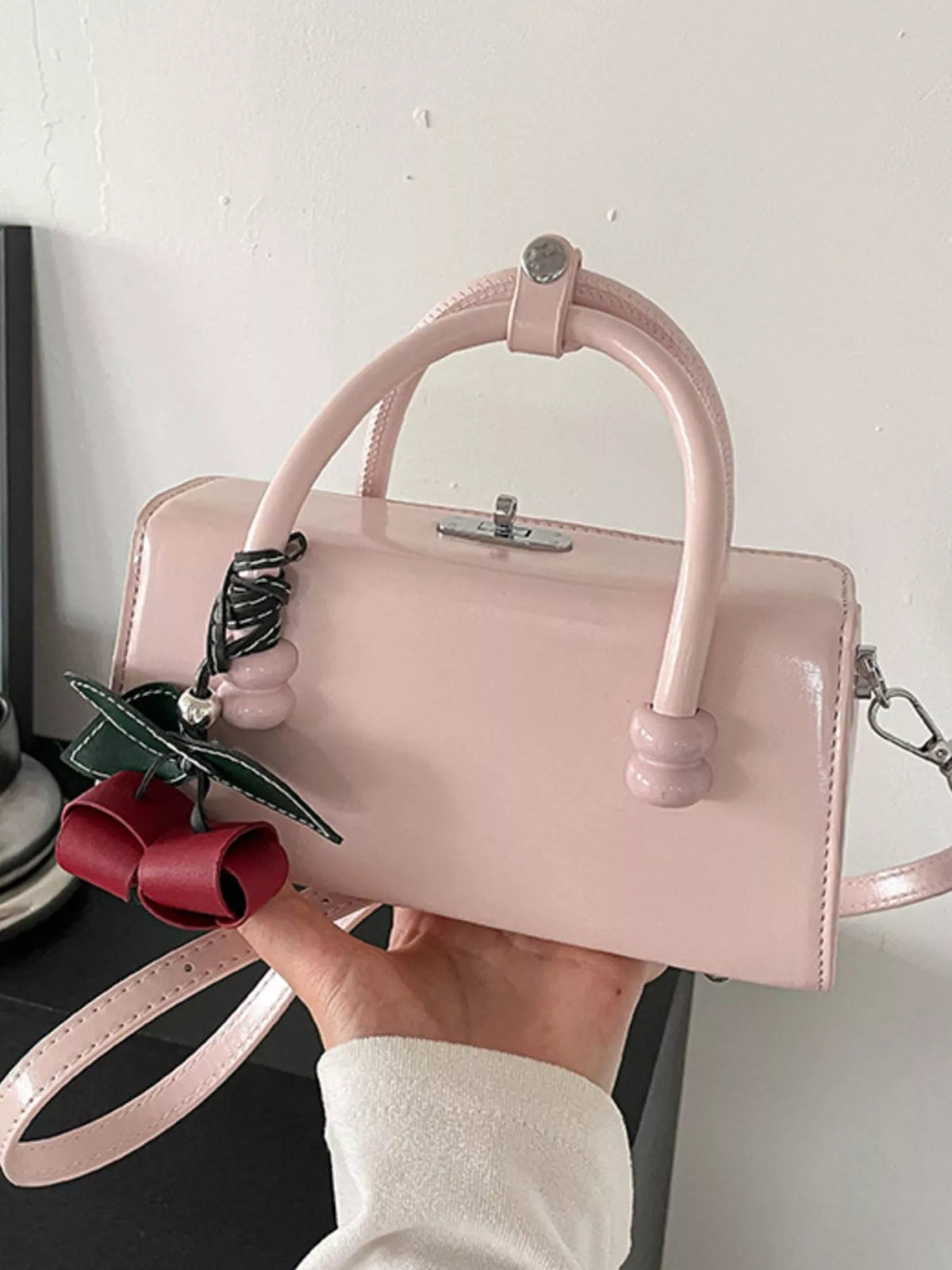 Light pink top-handle crossbody bag with rounded handles and red bow charm.