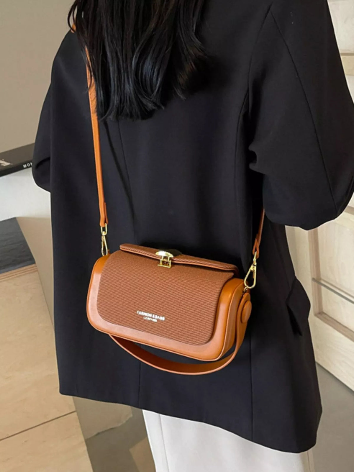 Brown flap crossbody bag with gold-tone clasp and adjustable strap on model
