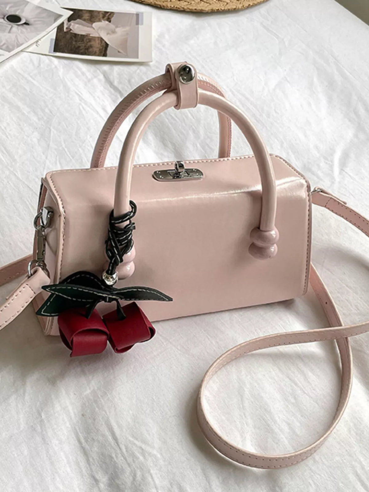 Light pink top-handle crossbody bag with crossbody strap and red bow charm.