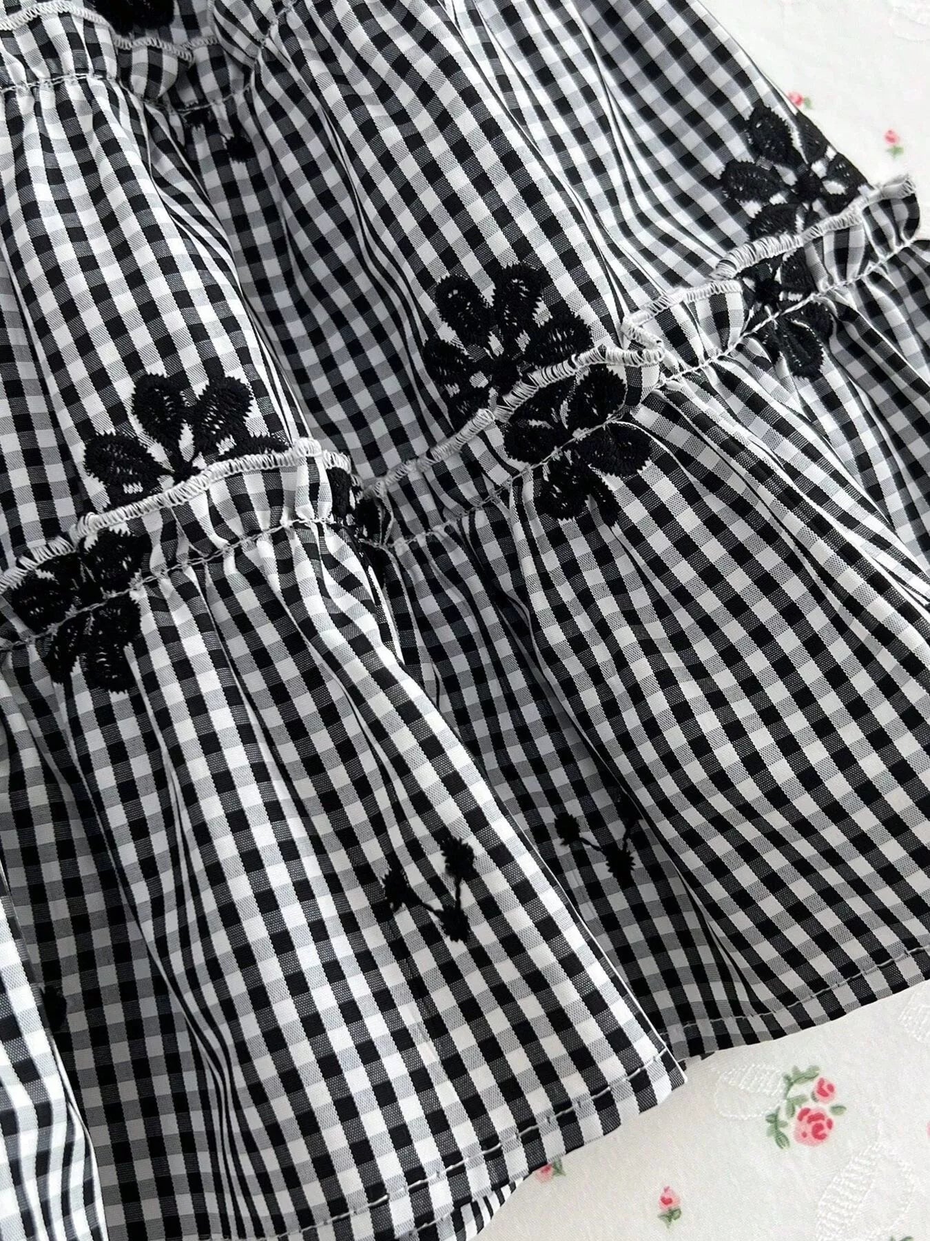 Close-up: black gingham tiered mini dress with embroidered floral ruffle details