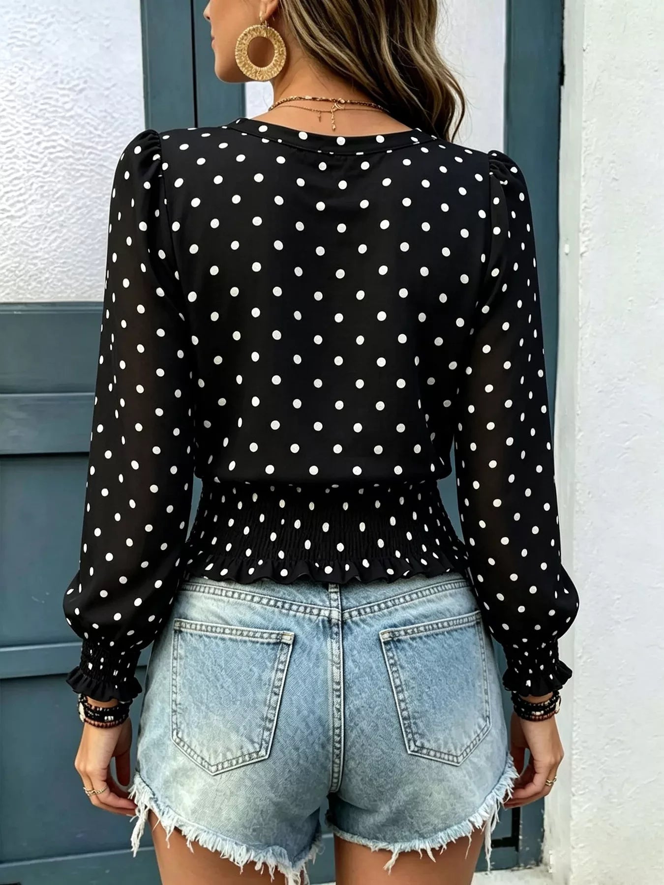 Back view of black polka dot long-sleeve smocked blouse with peplum ruffle hem