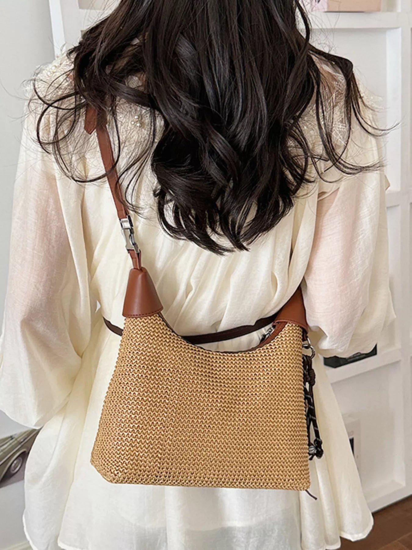 Small straw crossbody bag in tan with brown leather handle, worn crossbody with braided strap
