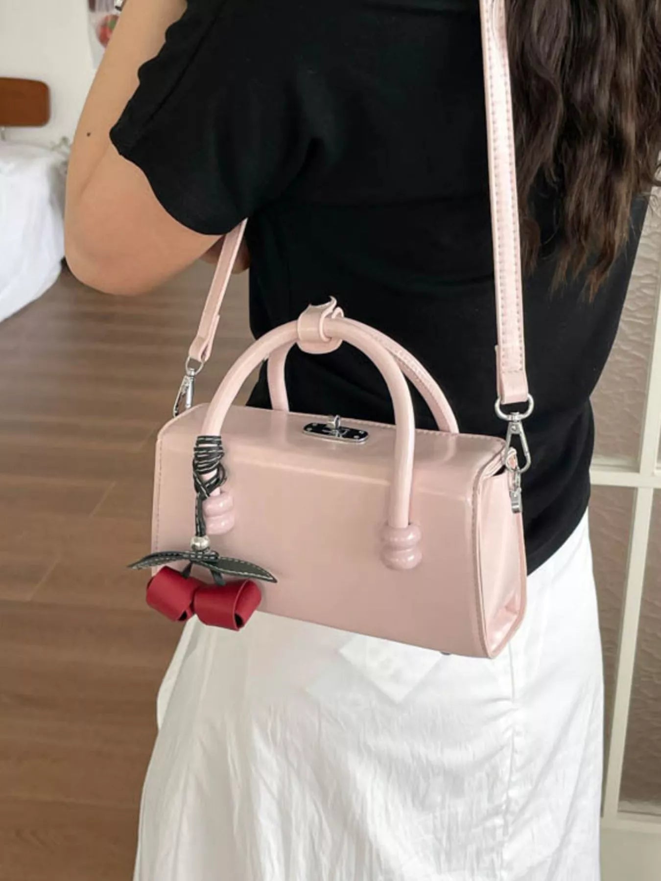 Pink top-handle crossbody bag with crossbody strap and red bow keychain charm.