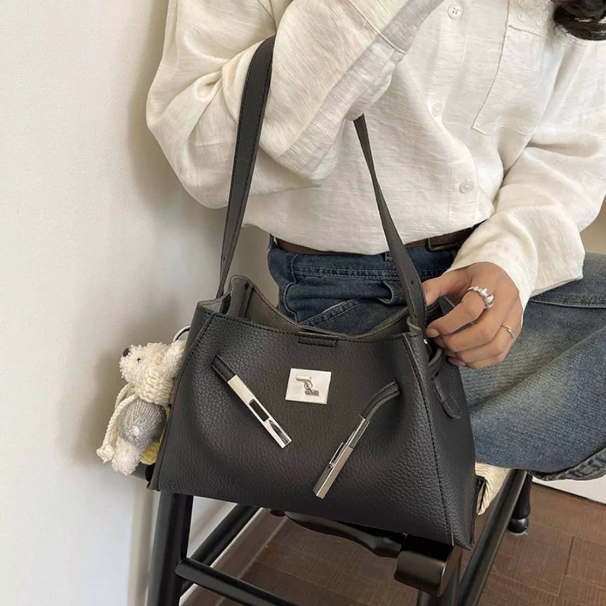Black lock-detail crossbody bag with silver bar accents, top zip, and teddy keychain
