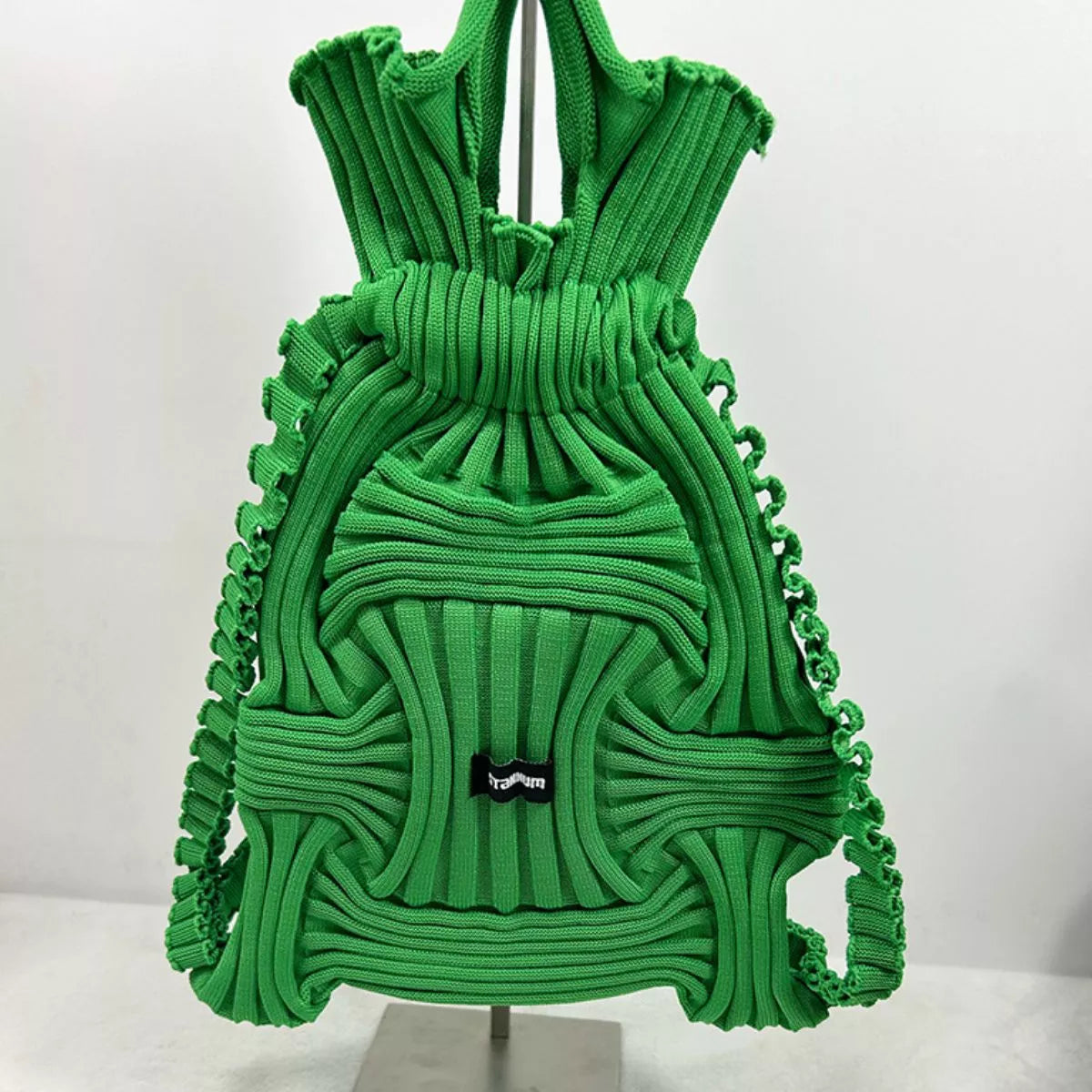 Green textured knit backpack with ruffled panels, top handles, front patch logo