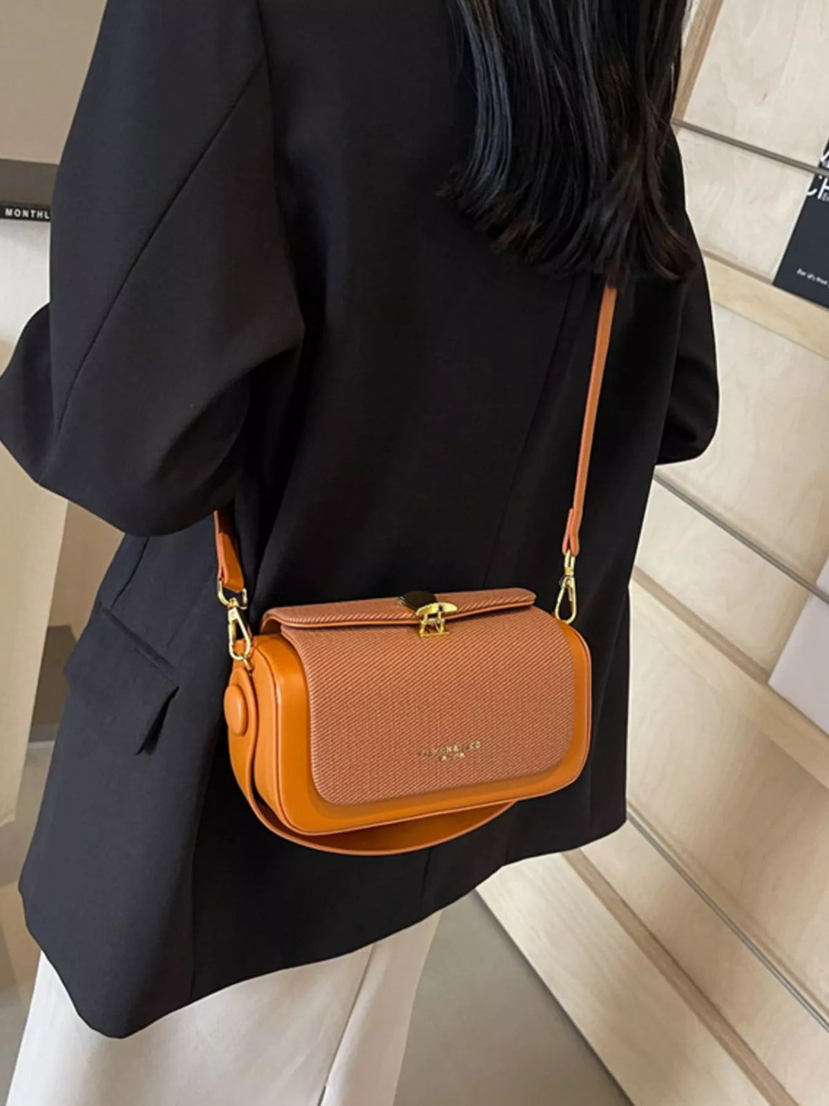 Brown flap crossbody bag with adjustable strap and gold-tone clasp on model