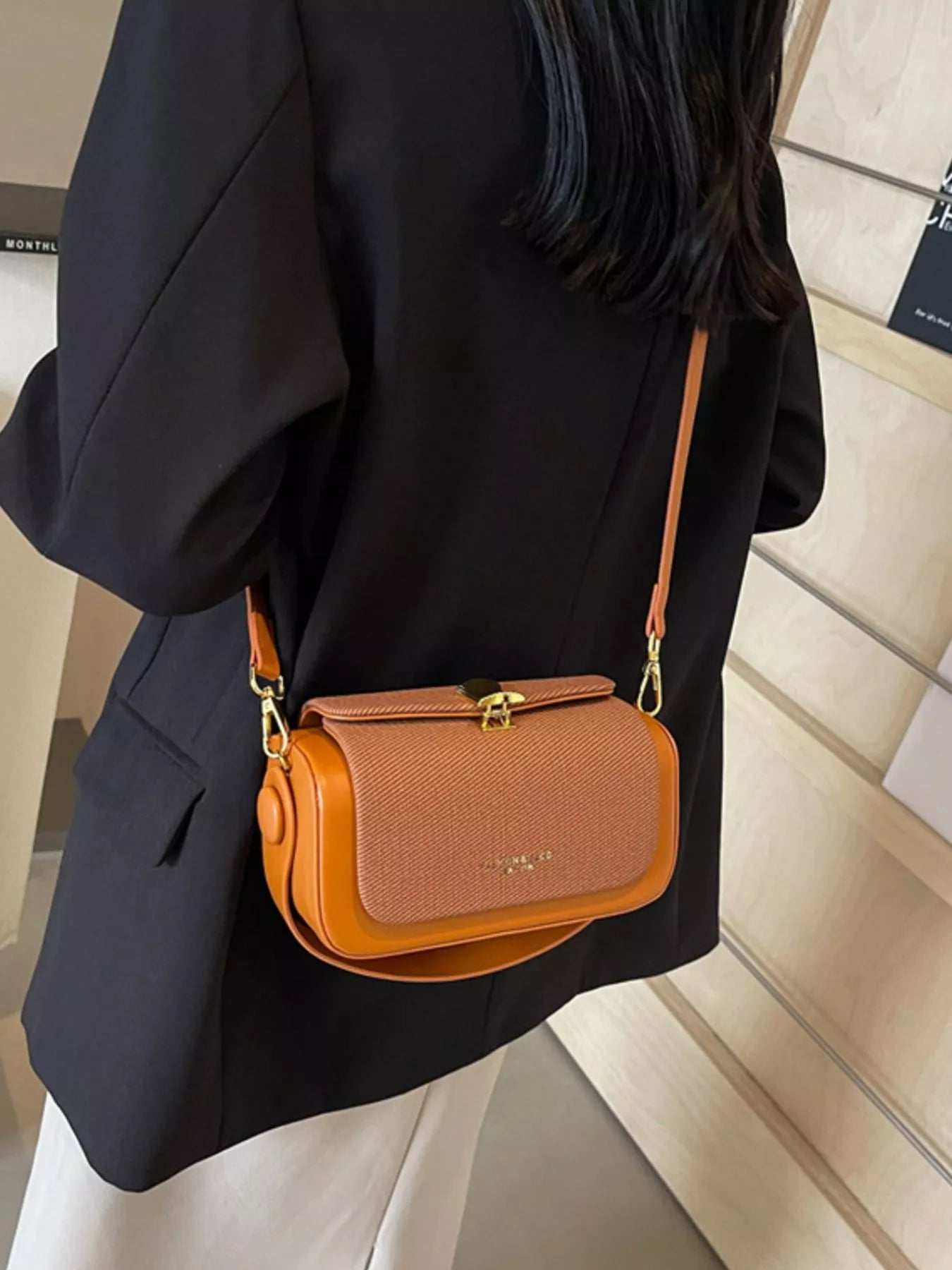 Brown flap crossbody bag with adjustable strap and gold-tone clasp on model