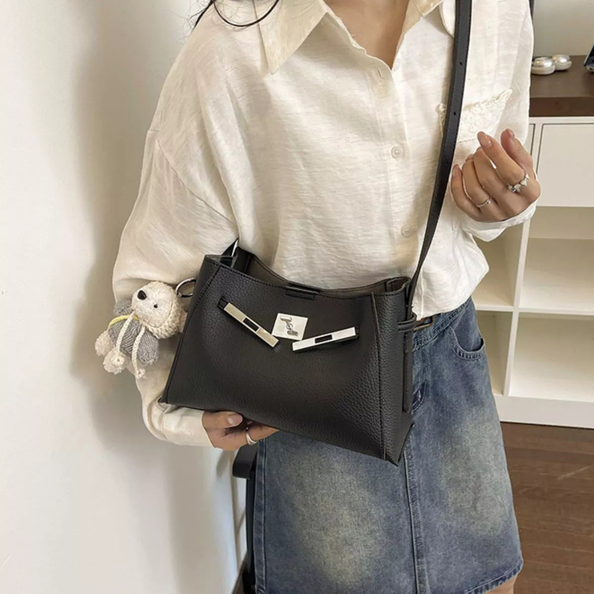 Black structured crossbody bag with top zip and silver lock hardware, worn with denim