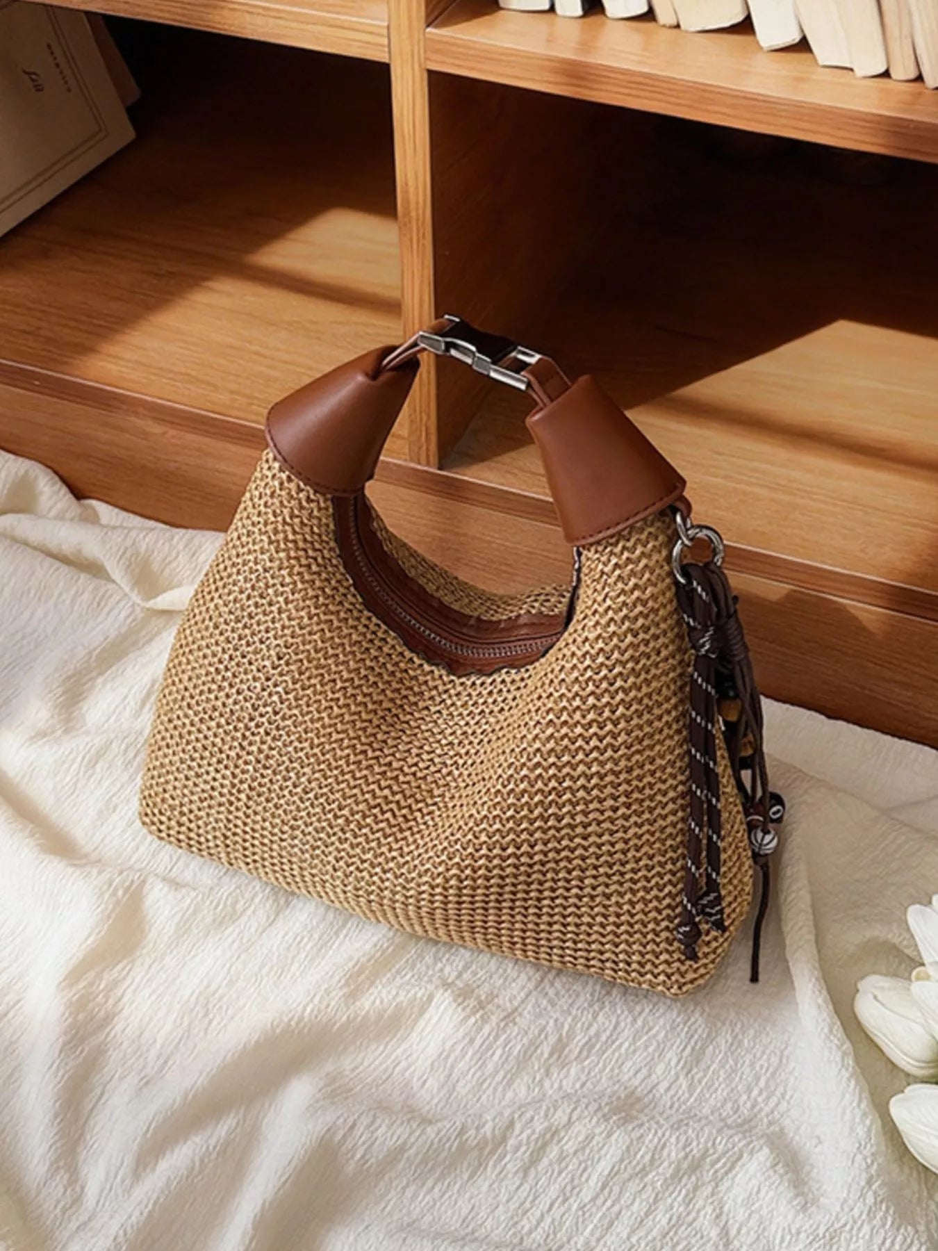 Woven straw crossbody bag with brown leather top handles and braided side tassel, structured shape