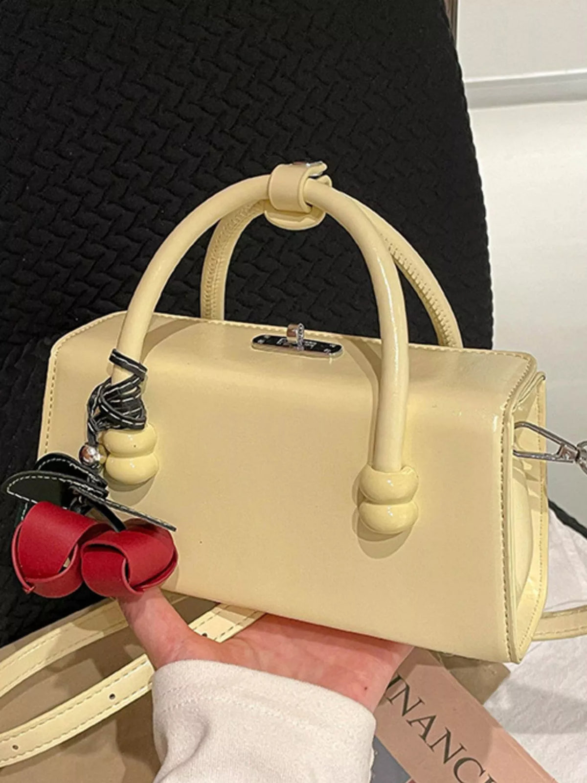 Yellow top-handle crossbody bag with silver clasp, curved handles, dangling ribbon charm