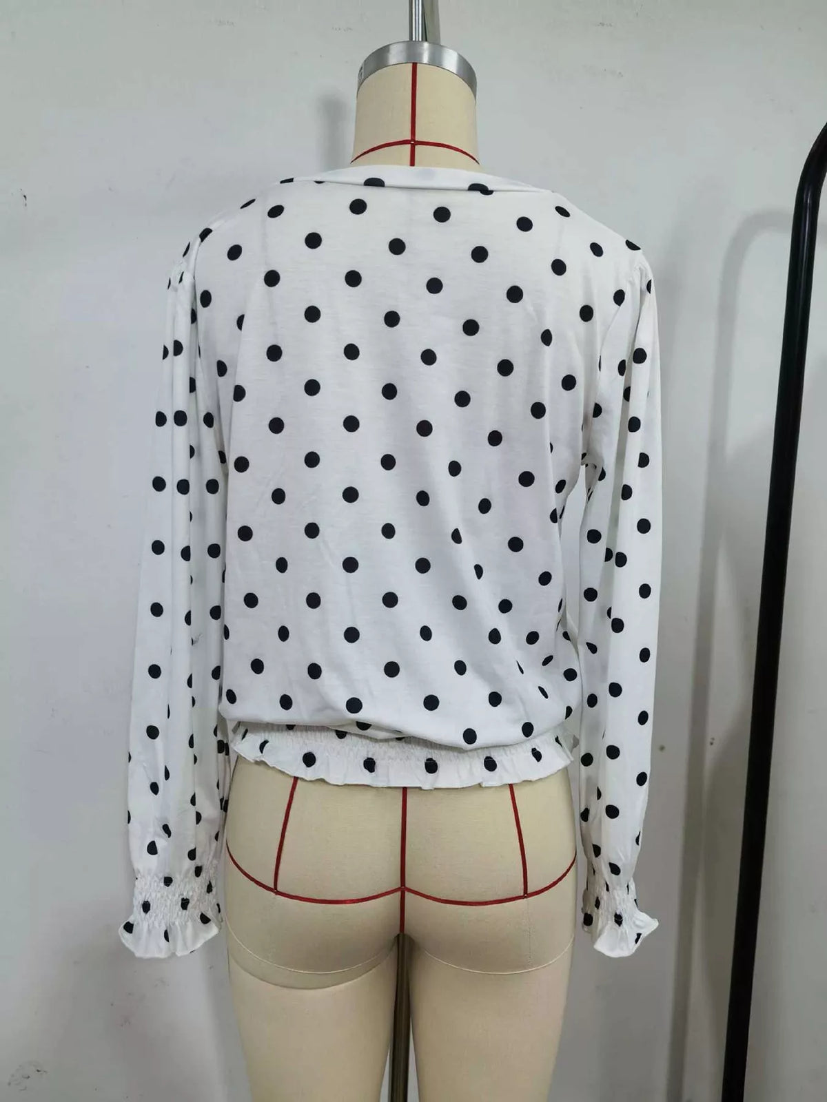 Back view of white polka dot V-neck blouse with long sleeves and ruffled hem