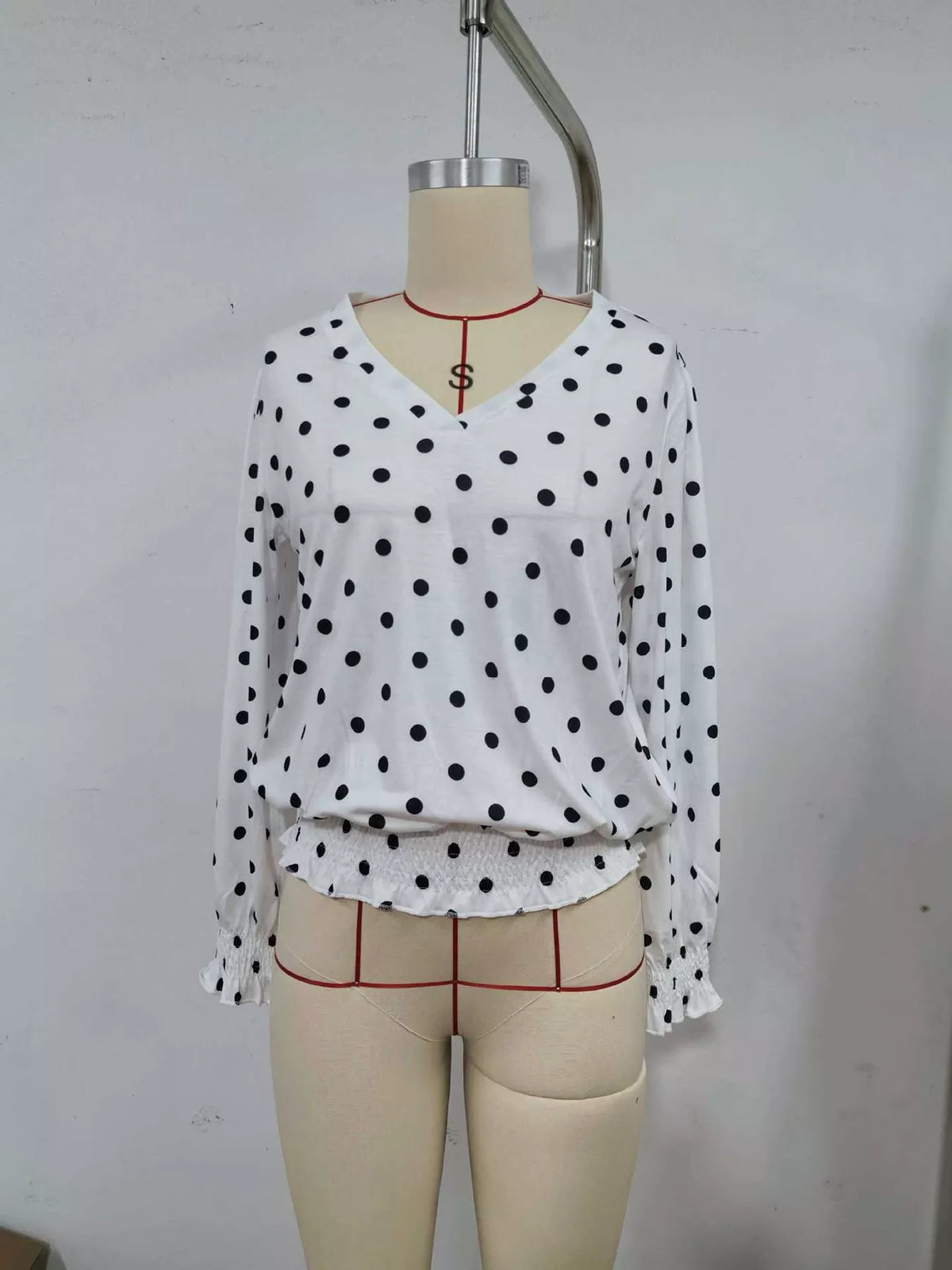 White polka dot V-neck blouse with long sleeves and gathered ruffle hem on mannequin