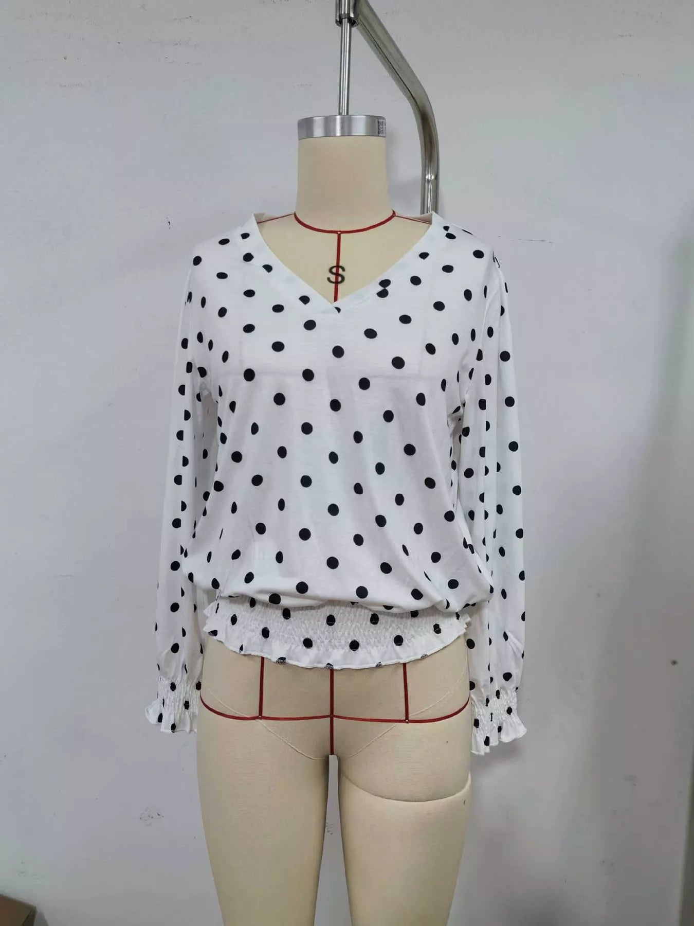White polka dot V-neck blouse with long sleeves and gathered ruffle hem on mannequin
