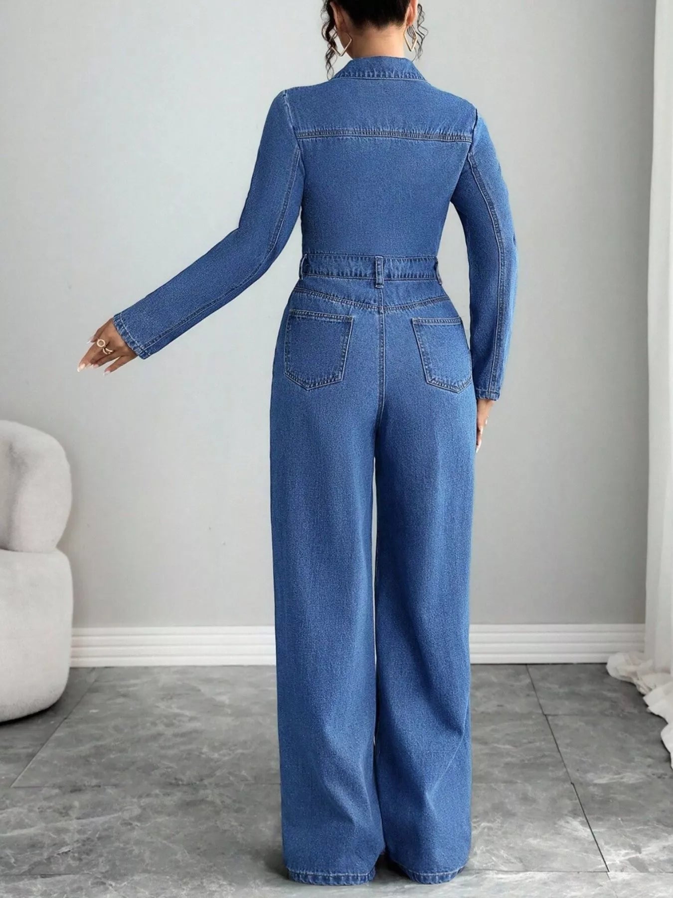 Back view: Blue denim long-sleeve button-front jumpsuit with yoke and rear pockets