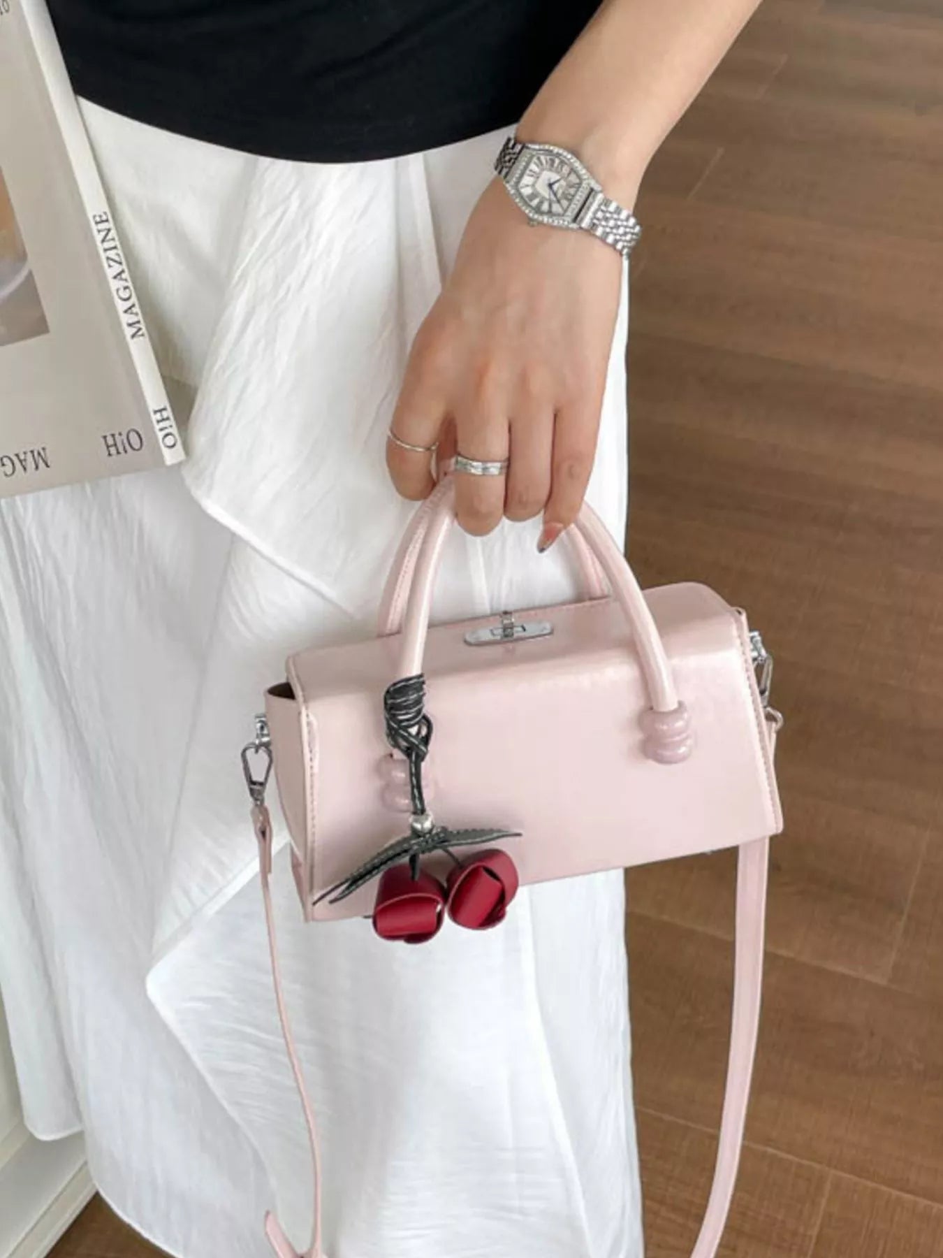 Light pink top-handle crossbody bag with long strap and red bow charm.