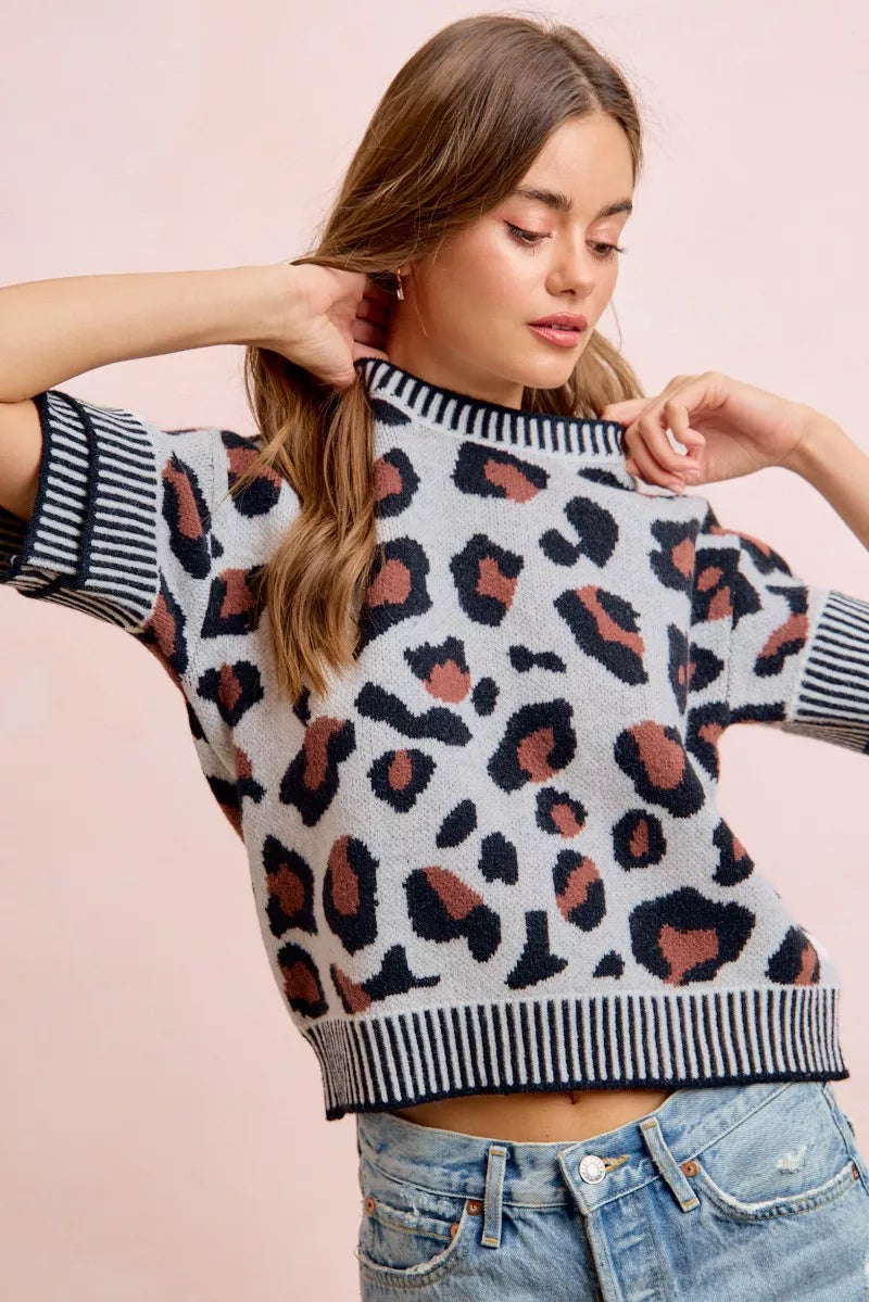 Leopard print knit top with striped crew neck and ribbed hem; arms raised pose.