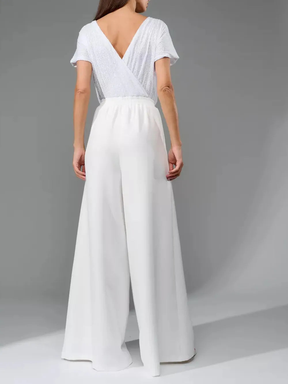 White jumpsuit with short sleeves, V-back wrap detail, and wide-leg pants.