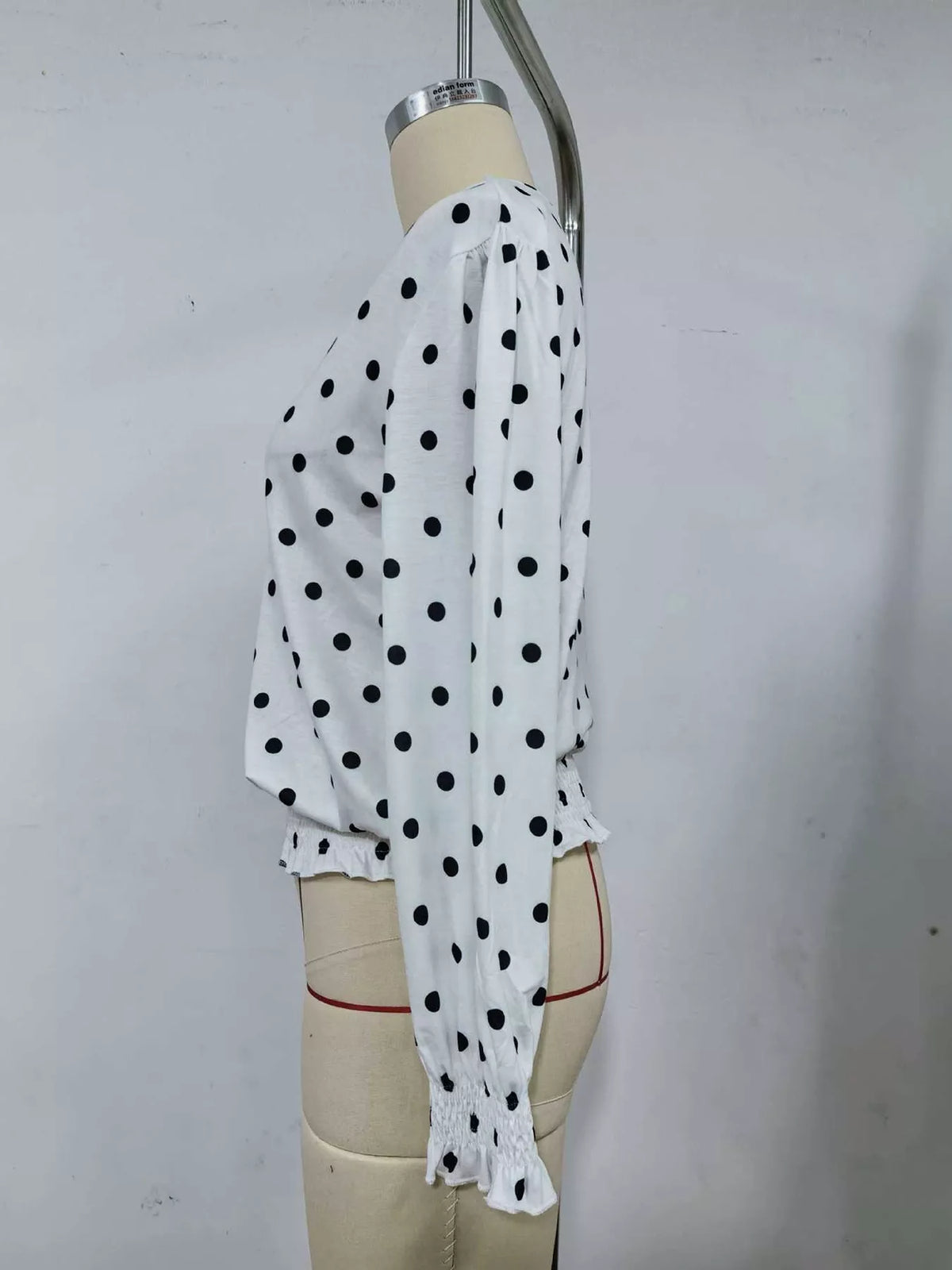 Side view of white polka dot smocked blouse with long sleeves and ruffled peplum hem