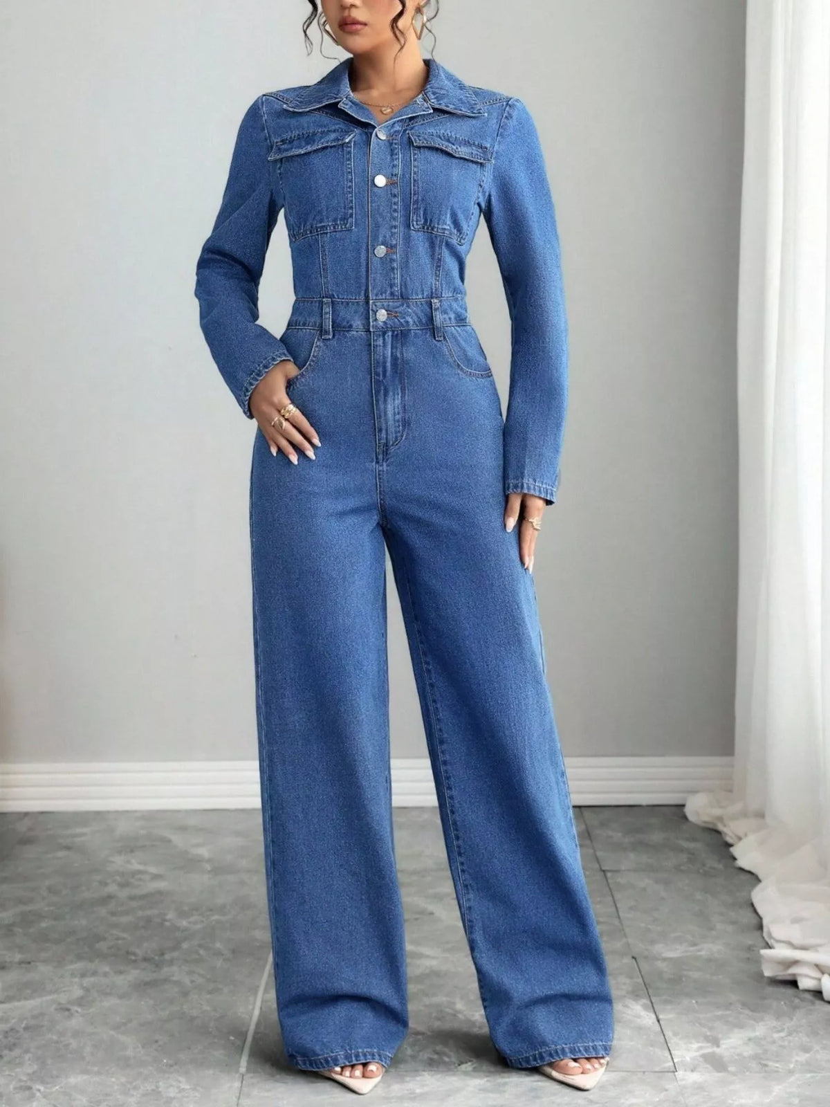 Blue denim long-sleeve jumpsuit with button front, chest pockets, belted waist seam