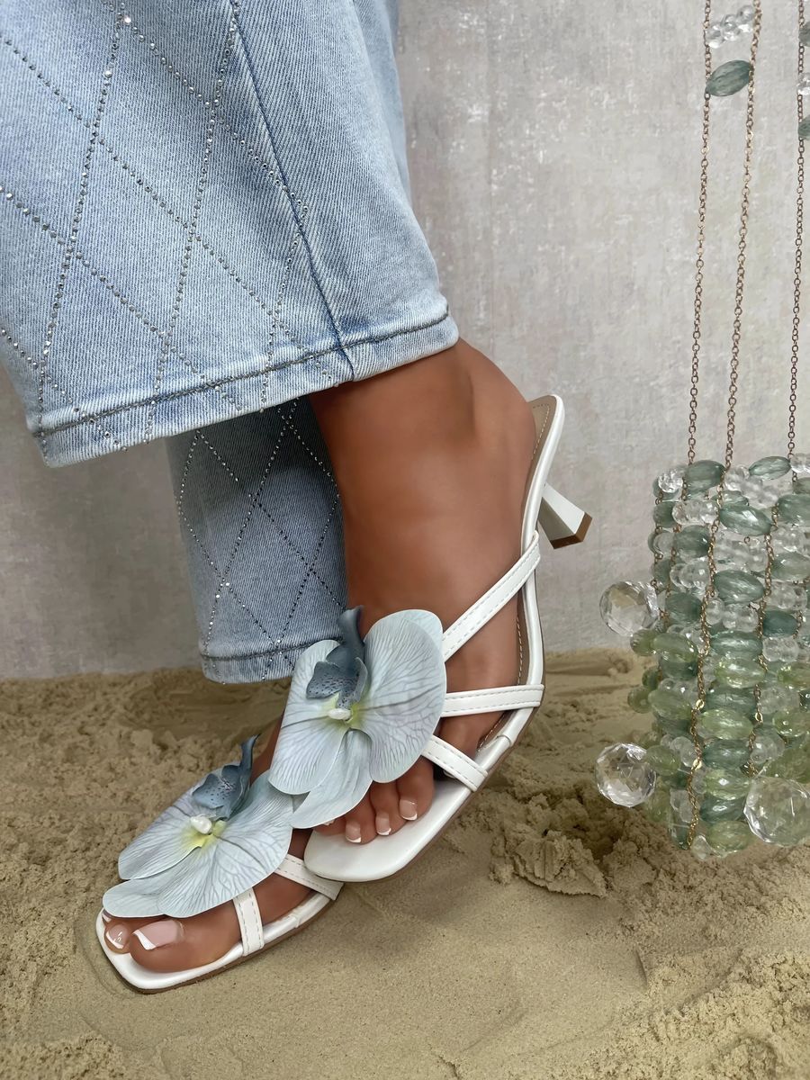 White strappy slide sandals with blue orchid flower embellishment and low heel