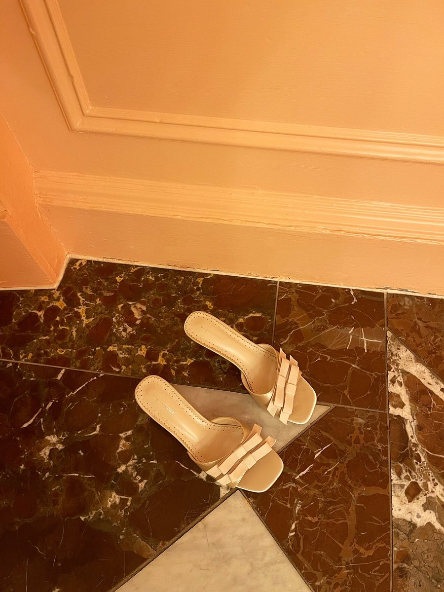 Cream open-toe high heel sandals with bow detail, placed on the floor