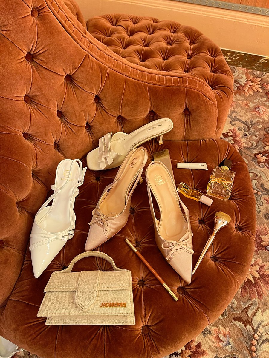 Cream open-toe high heel sandals with bow detail, styled on velvet seat