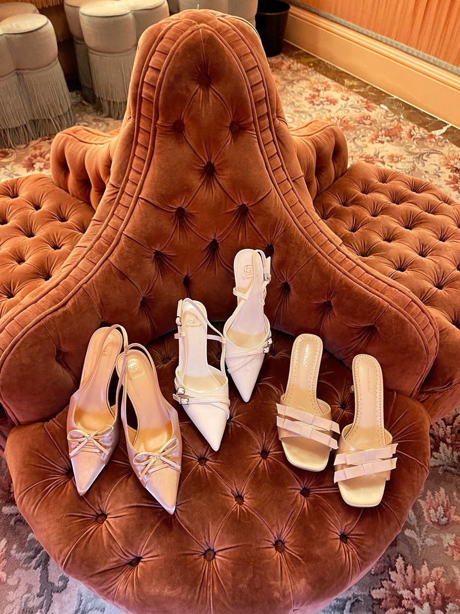Cream open-toe high heel sandals with bow detail, multiple pairs on chair