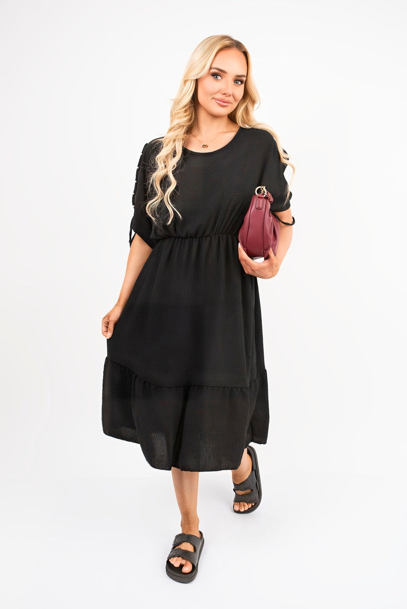 Black round neck midi dress with short sleeves and tie detail at cuffs, tiered hem