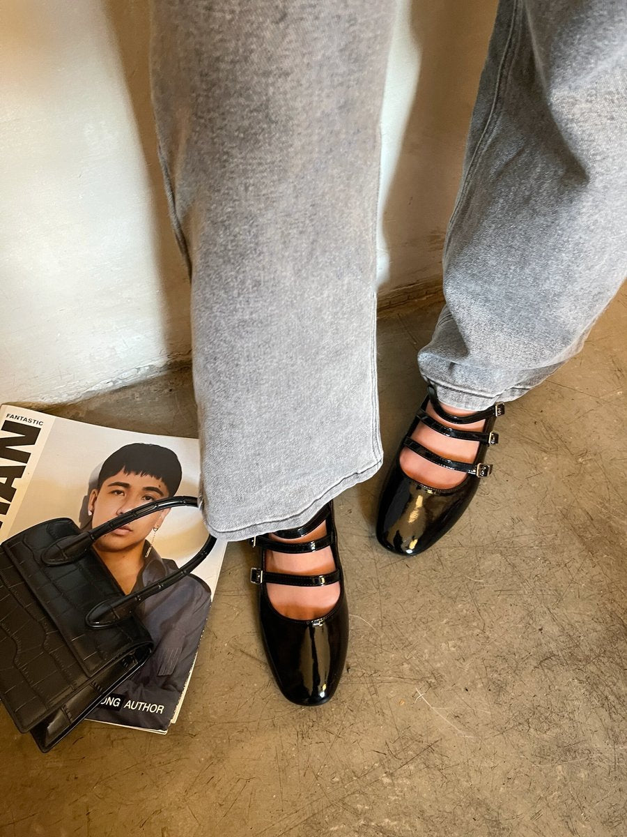Black strappy flat shoes with multiple buckles and glossy finish, worn with jeans